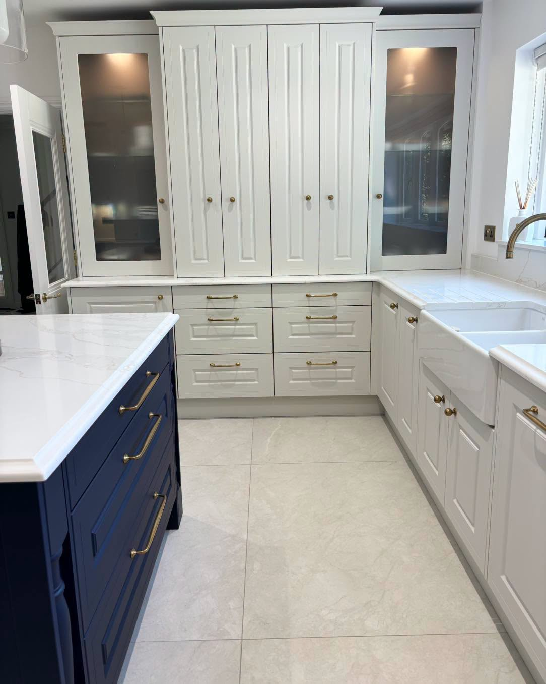 Bright modern kitchen with white cabinetry, blue island, and large white-tiled floor.