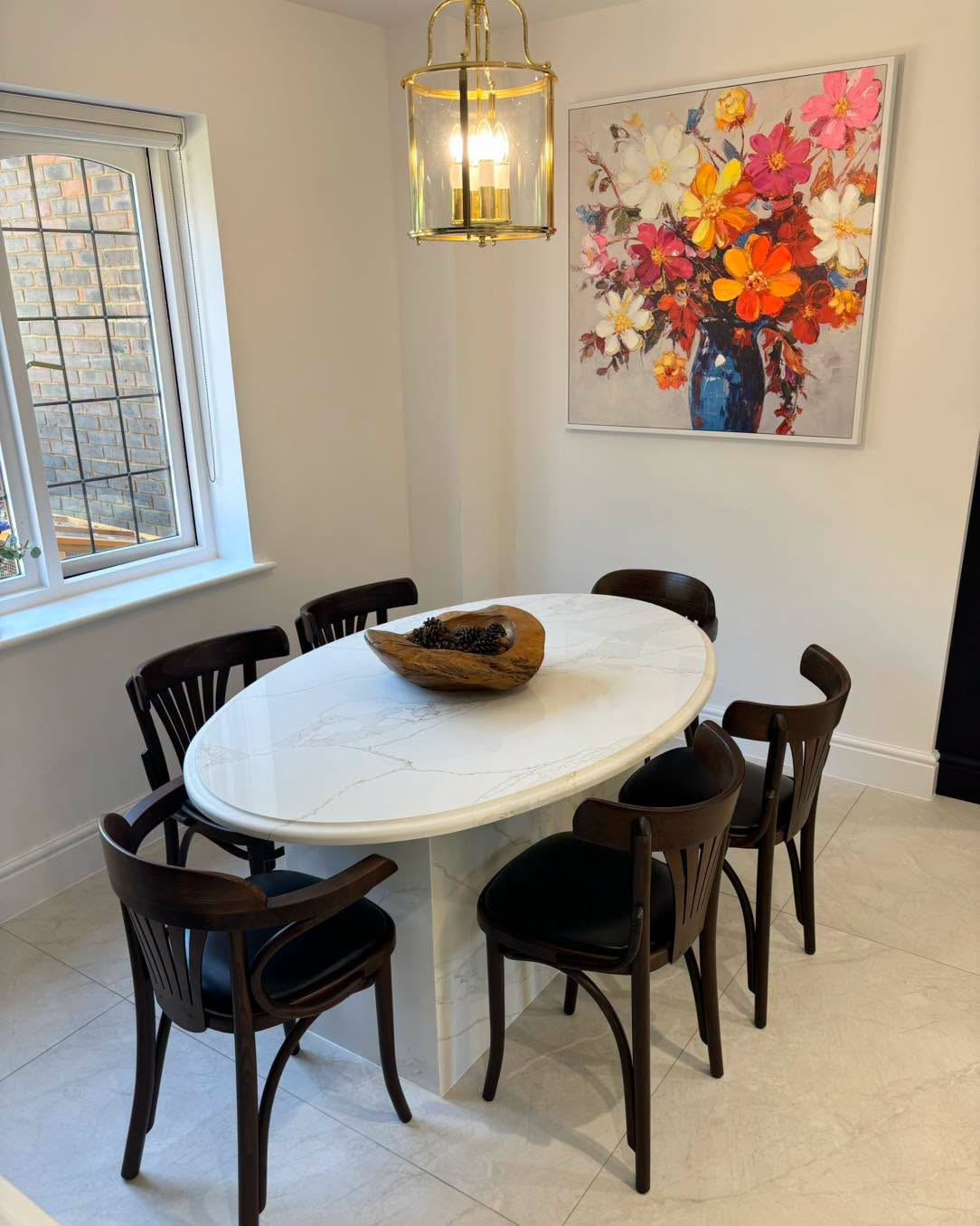 Dining nook with oval white table, dark chairs, floral wall art, and a hanging pendant light.