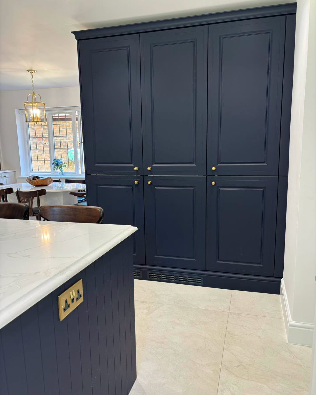 Navy blue built-in cabinets in a bright kitchen with white countertops and beige tile floor