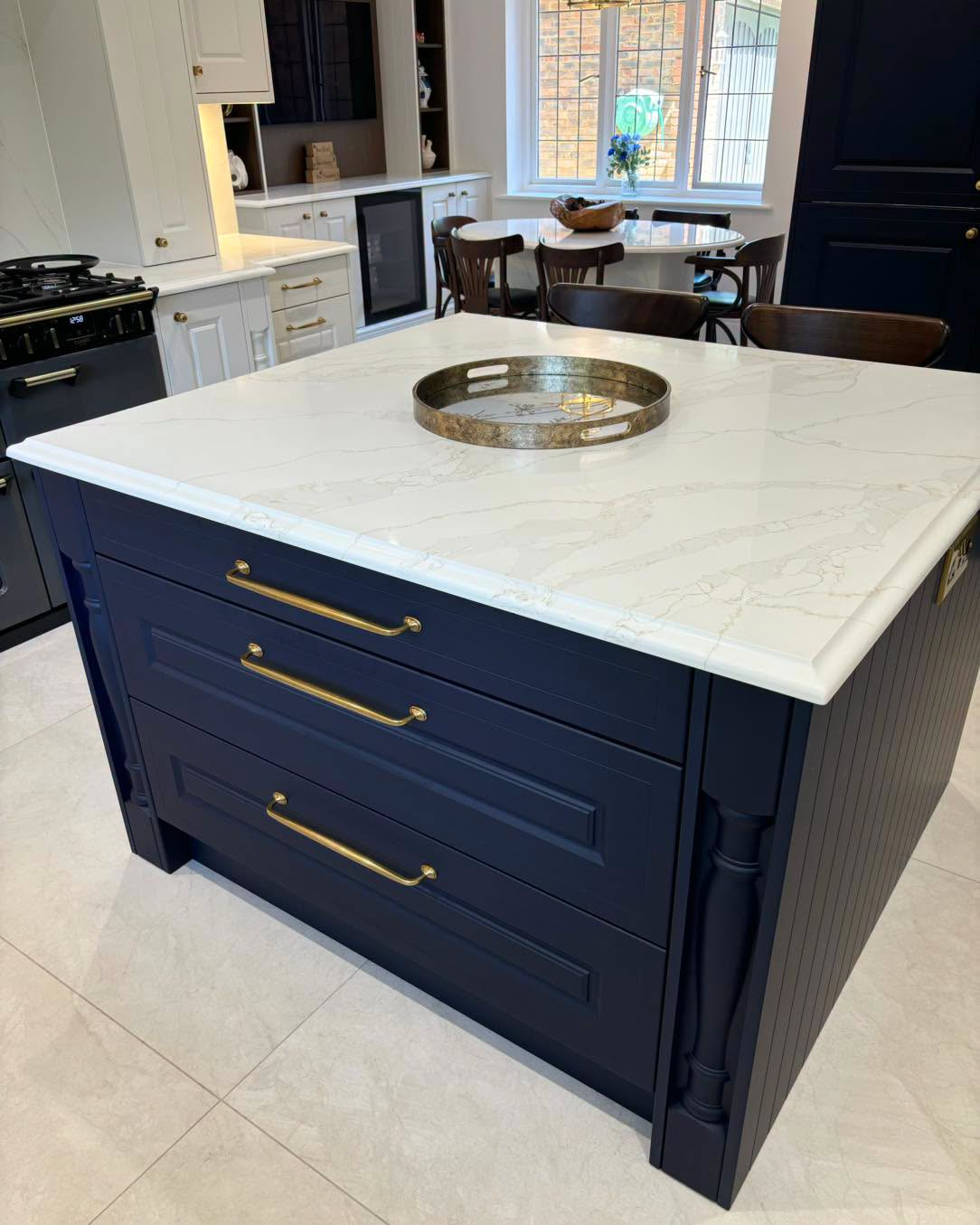 Navy kitchen island with white marble countertop and brass handles in a bright modern kitchen