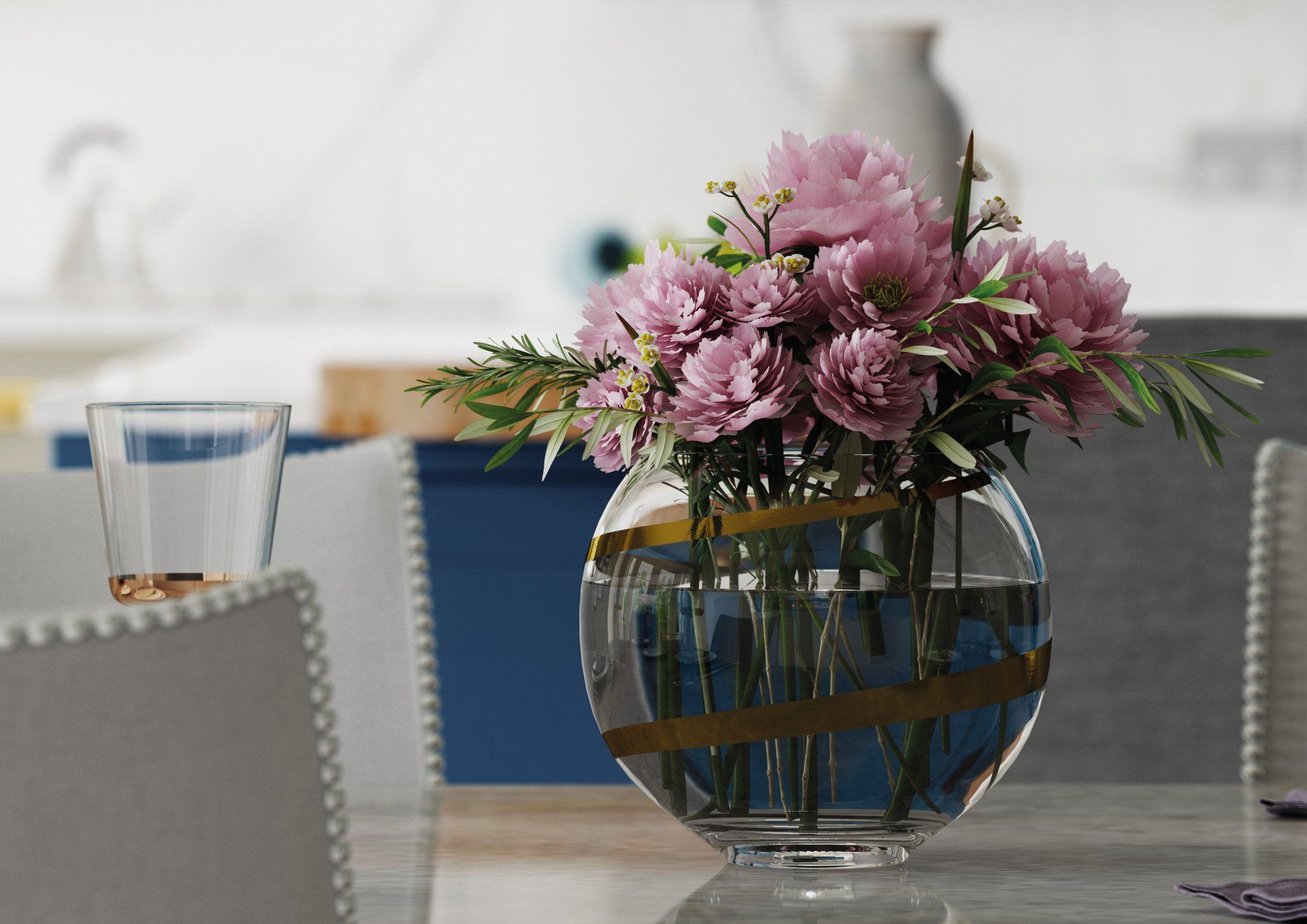 A clear, round glass vase with gold-tone stripes holds a bouquet of light purple flowers on a table.
