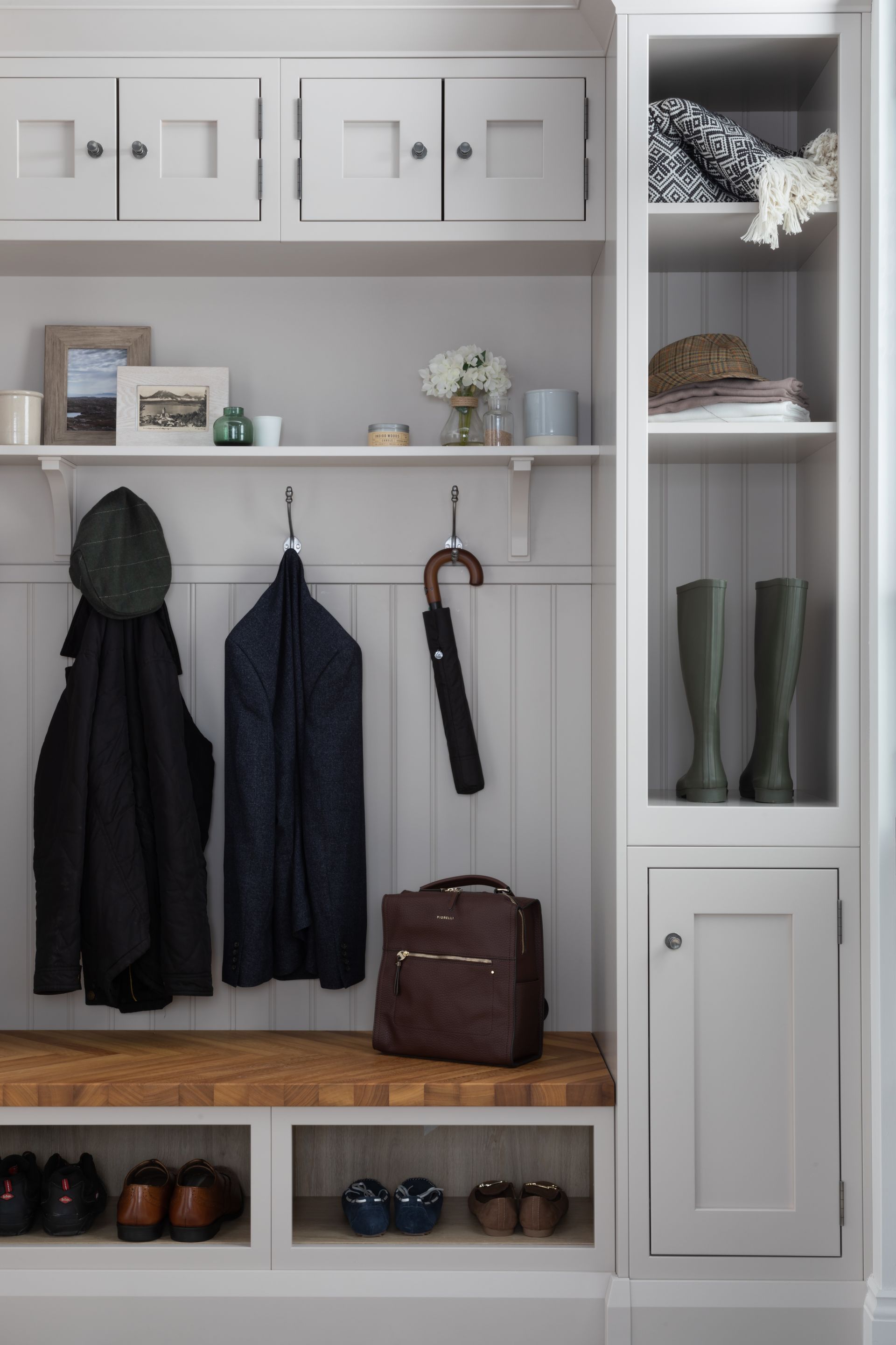 A white mudroom built-in with a wood bench, coat hooks, storage cabinets, open shoe cubbies, and a tall display shelf.