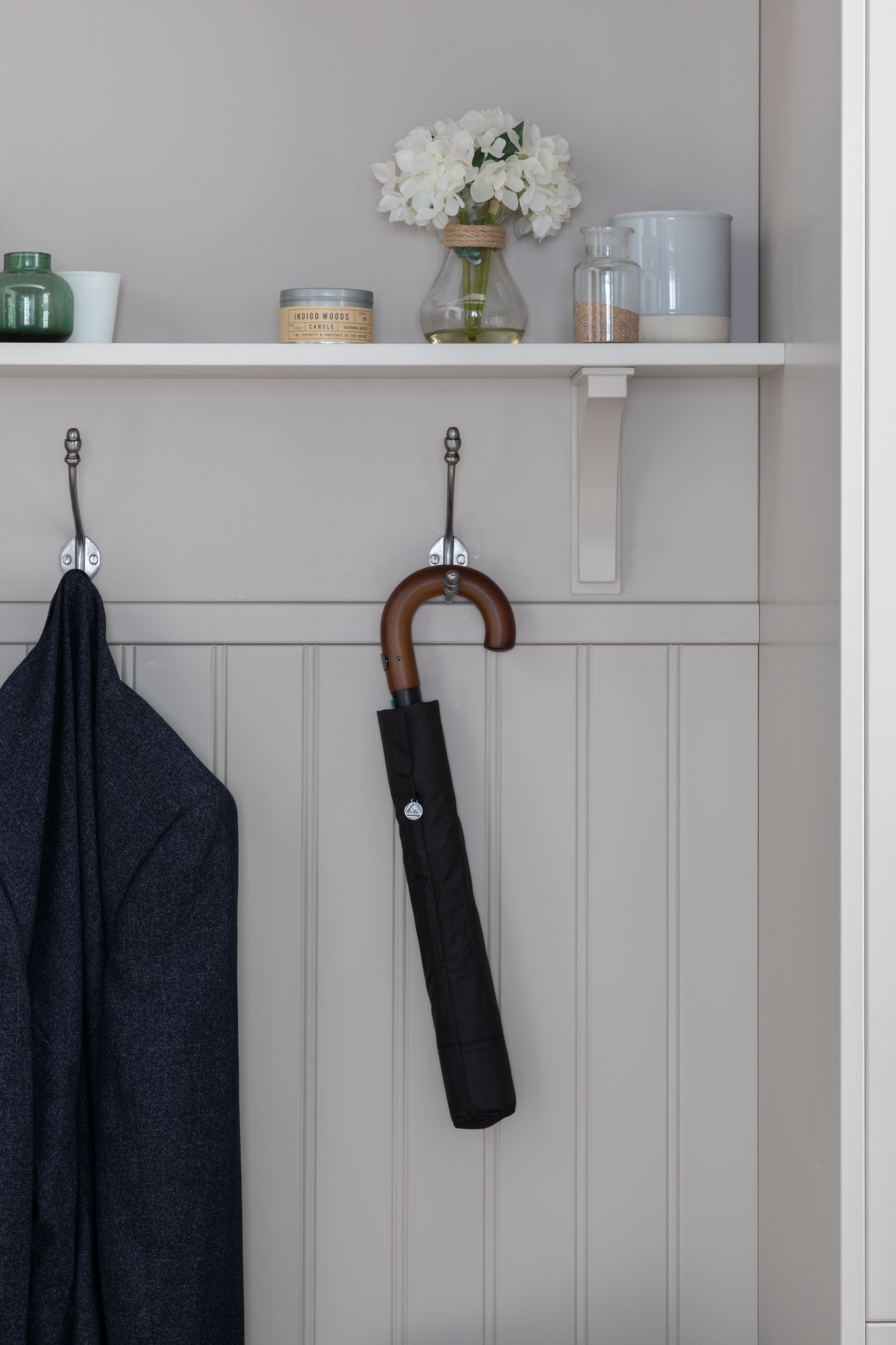 A coat rack with a hanging coat and an umbrella, featuring a shelf above holding flowers and decorative items.