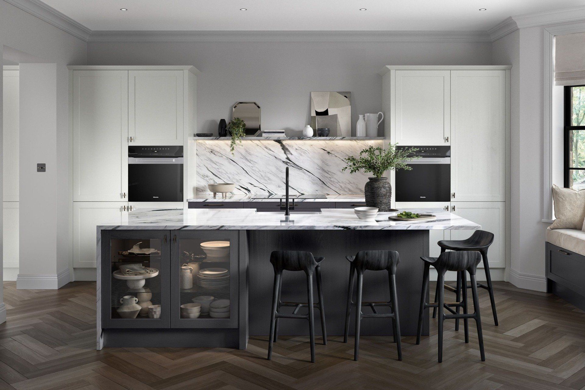 A modern kitchen featuring a dark island with bar stools, white cabinetry, integrated ovens, and a marble backsplash.