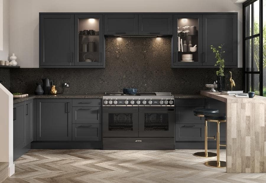Modern dark gray kitchen with a range oven, herringbone wood floor, and a small breakfast bar with two stools.