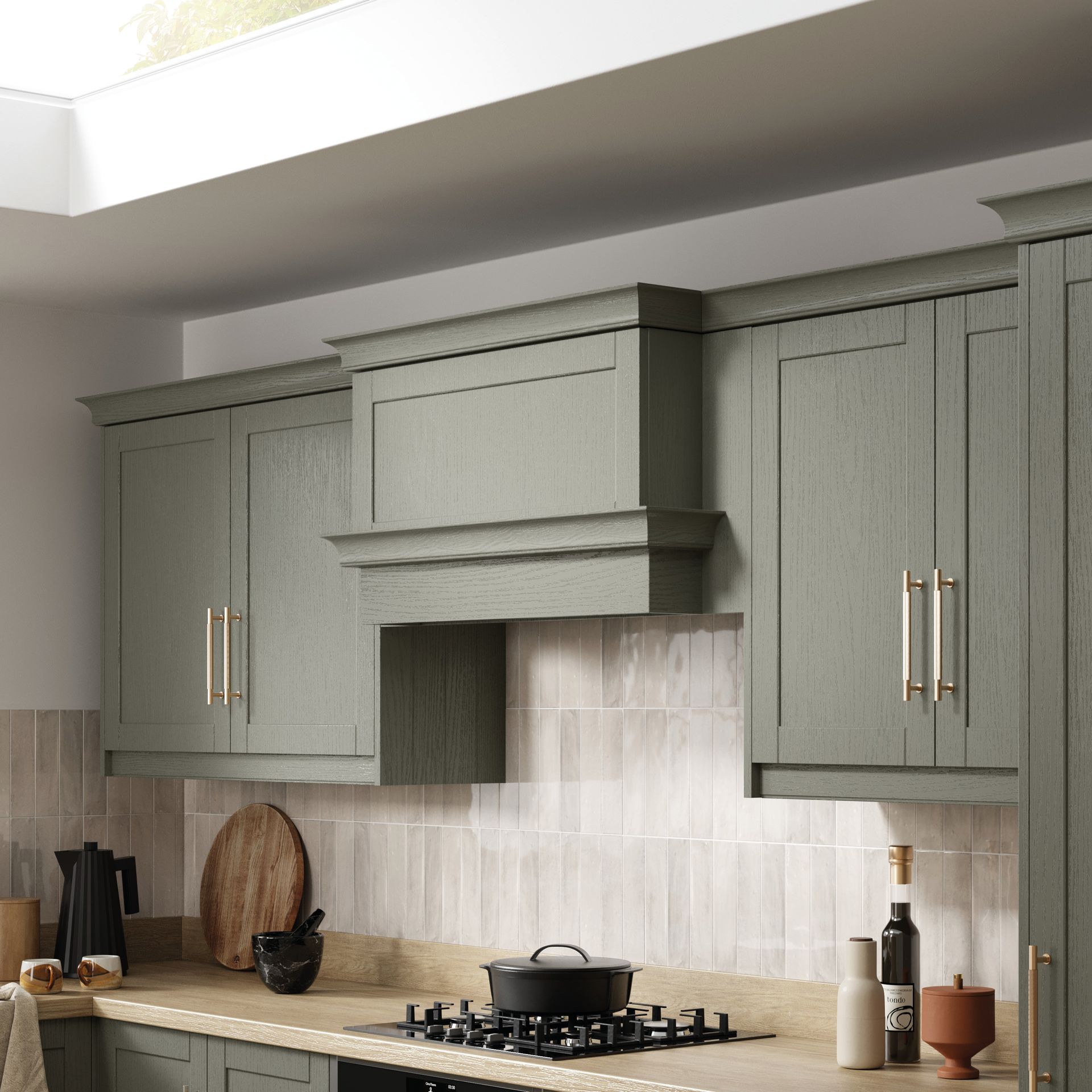 Sage green kitchen cabinets with a range hood over a stove, featuring gold hardware and a light-colored tile backsplash.