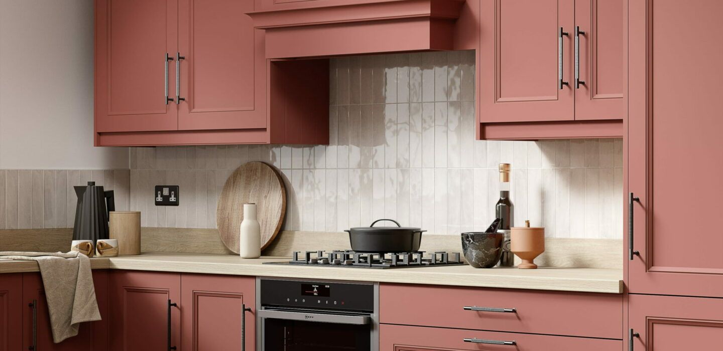 A kitchen with dusty pink cabinets, a light wood countertop, a stainless steel oven, and a tiled backsplash.