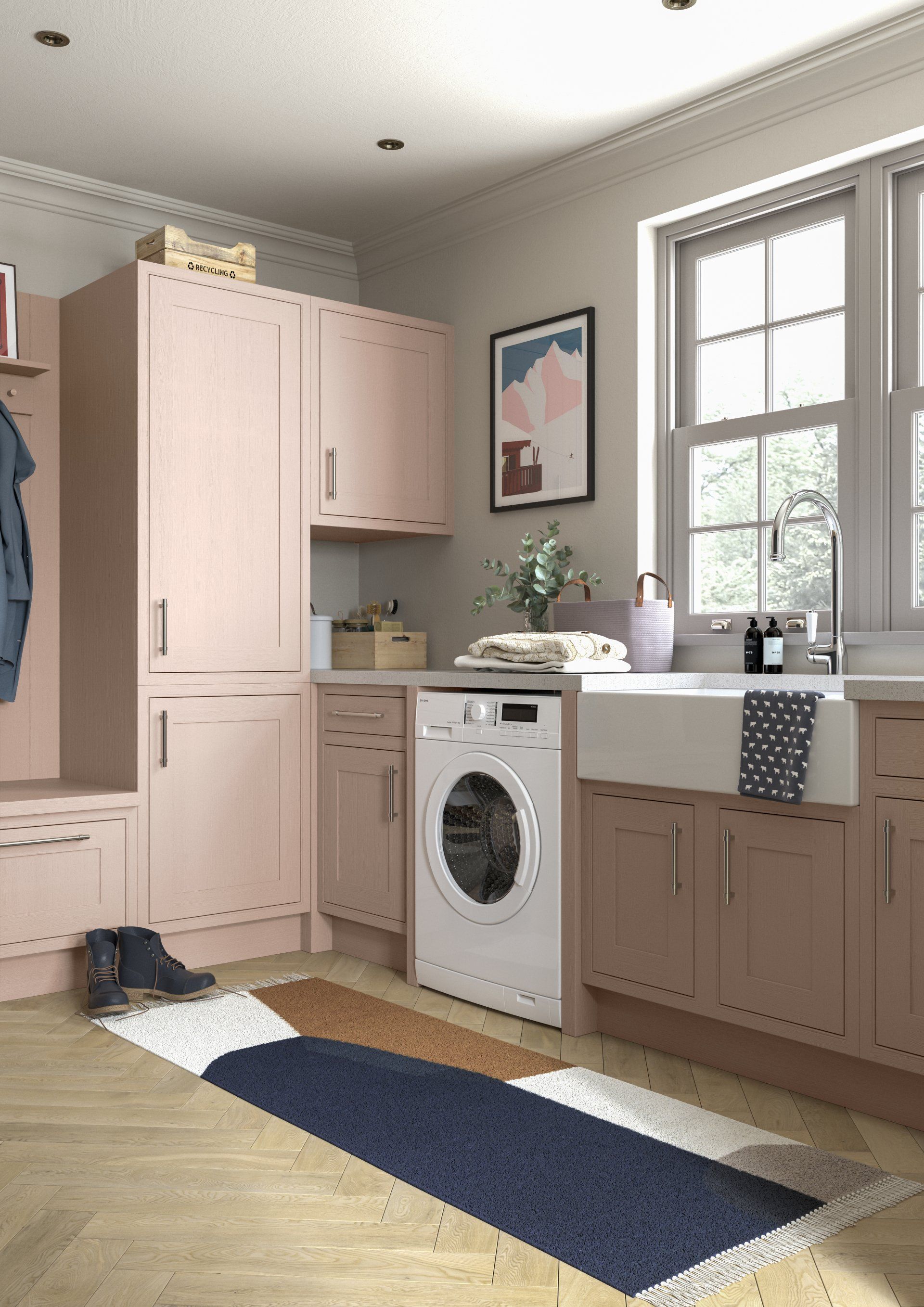 A laundry room with soft pink cabinets, a white front-load washing machine, a farmhouse sink, and a colorful runner rug.