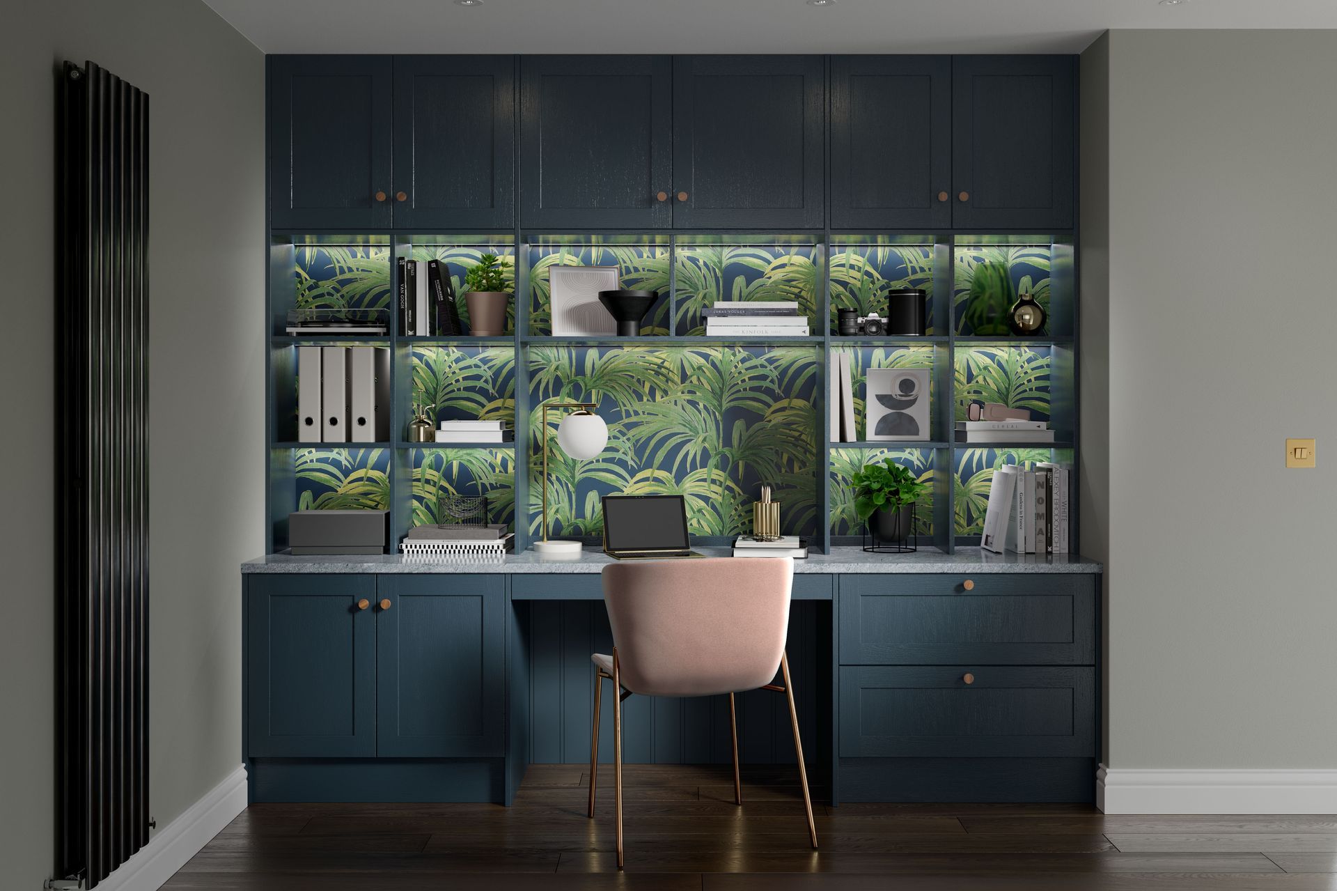 A home office featuring a desk with dark blue cabinets, gold hardware, tropical wallpaper, and a blush pink velvet chair.
