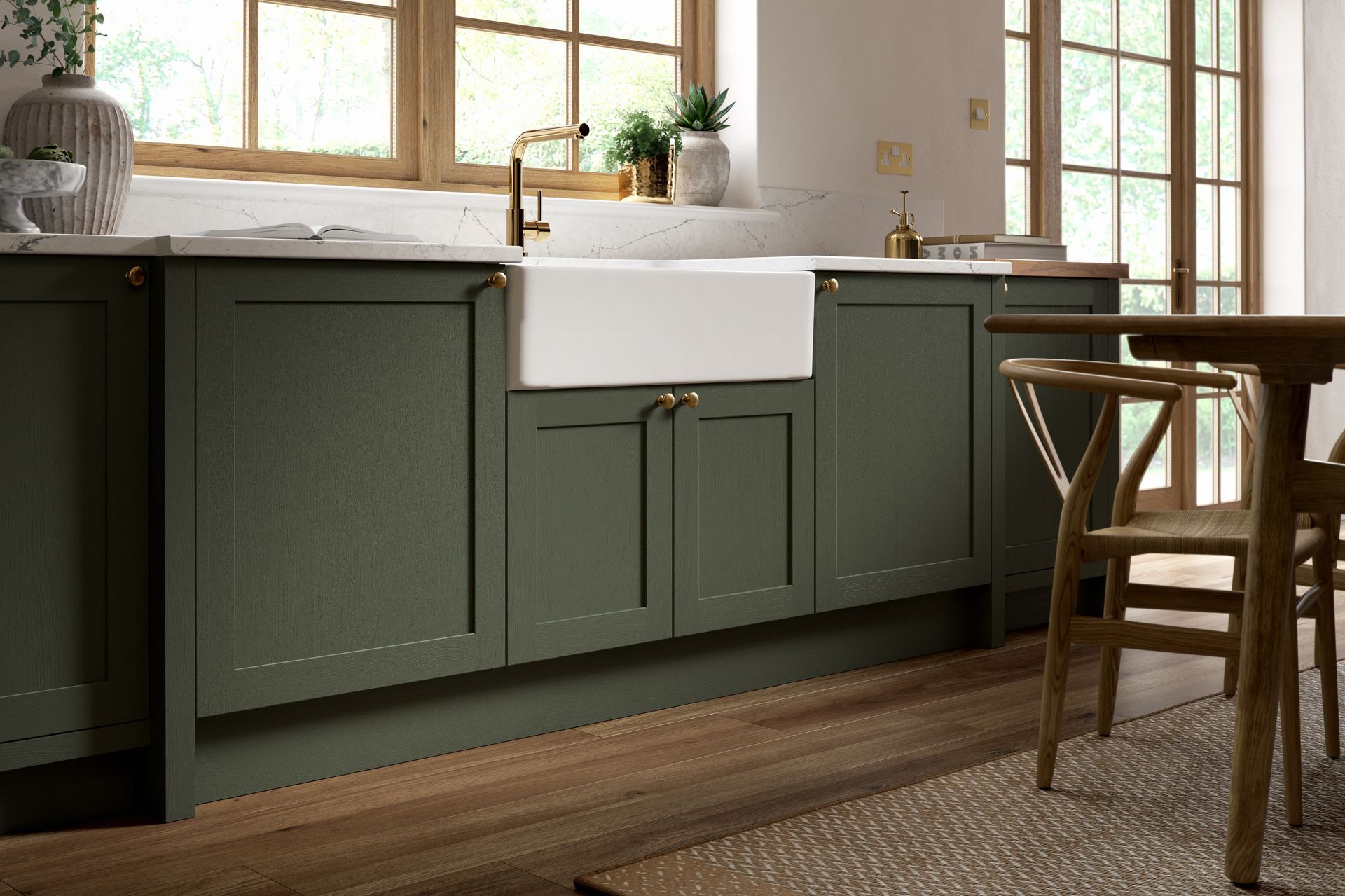 A sage green kitchen island featuring a white farmhouse sink, brass faucet, and wooden chair on a wooden floor.