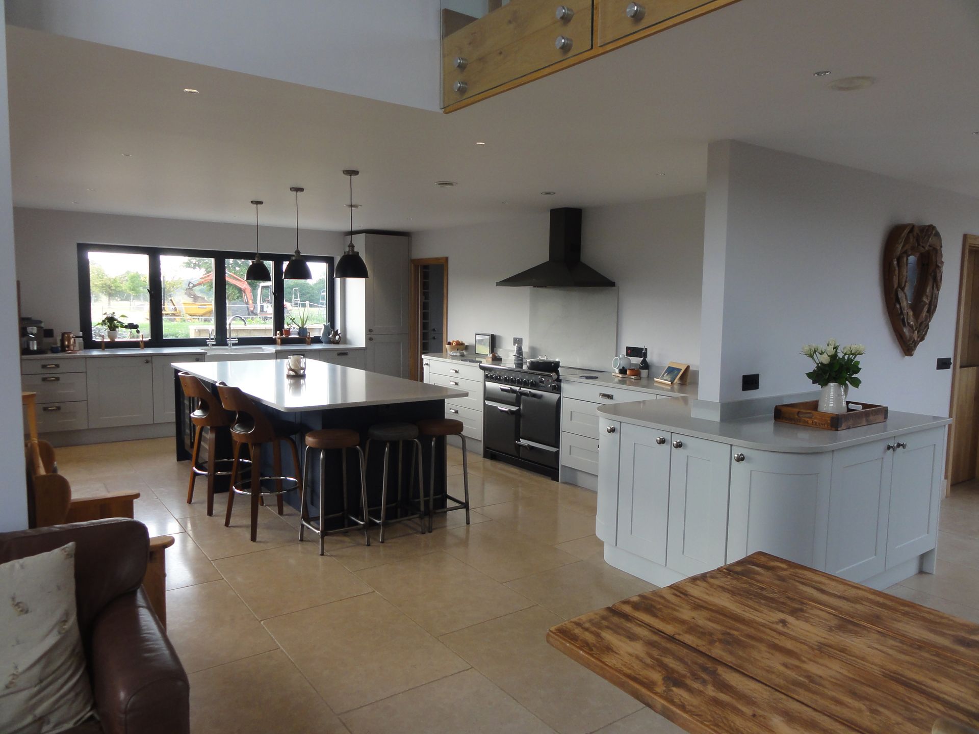 A spacious, open-plan kitchen with a large dark island, light cabinets, a black stove, and windows overlooking a field.