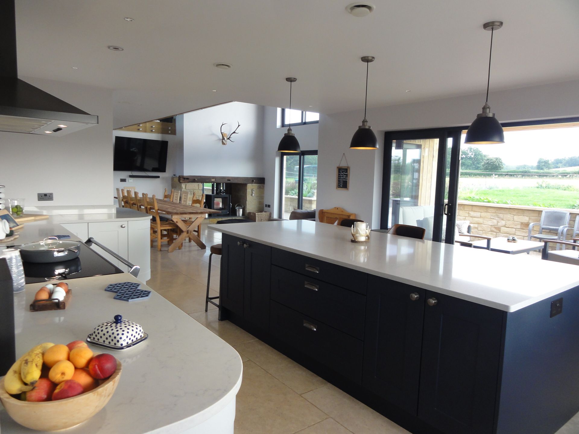 Modern kitchen with a large dark blue island, white countertops, three pendant lights, and a view of an outdoor patio.
