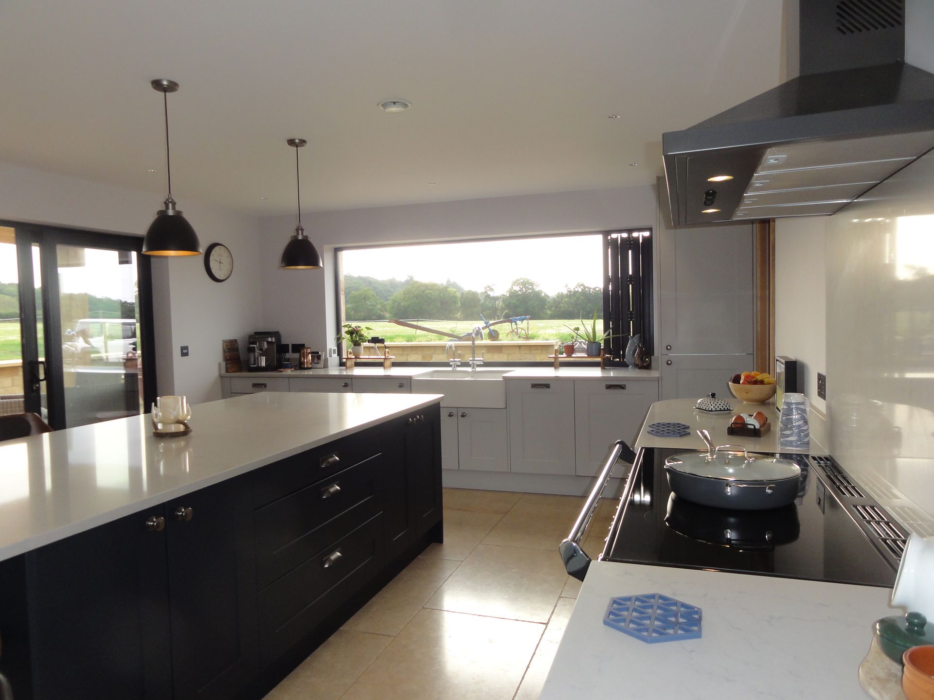 Modern kitchen featuring a large dark island, white cabinets, and a wide window overlooking a scenic countryside view.