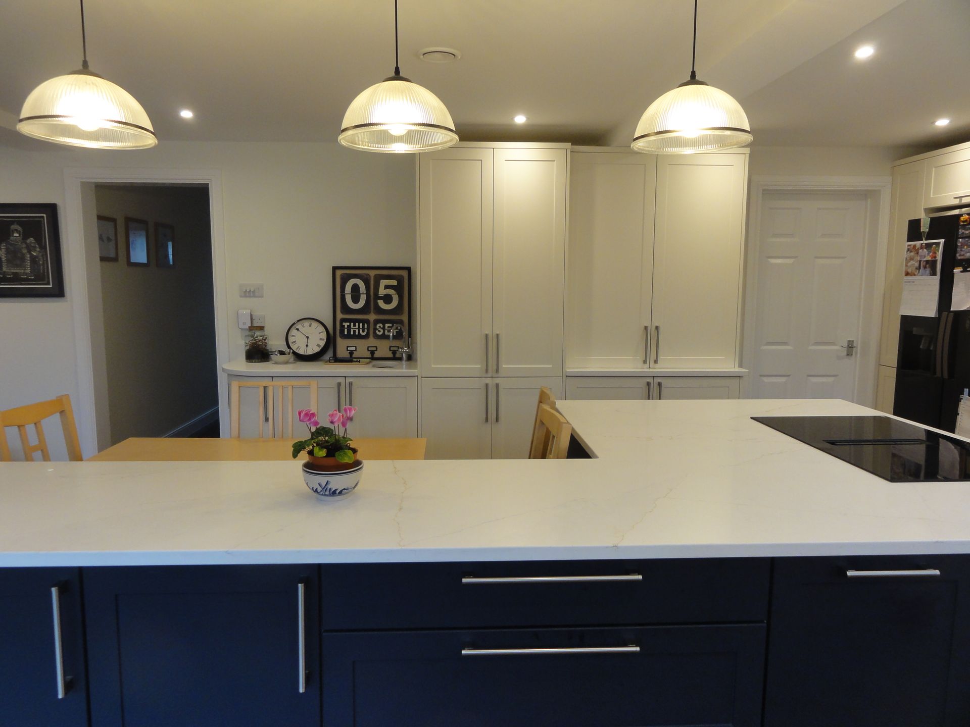 Modern kitchen with a dark blue island, white countertops, hanging pendant lights, and floor-to-ceiling white cabinetry.