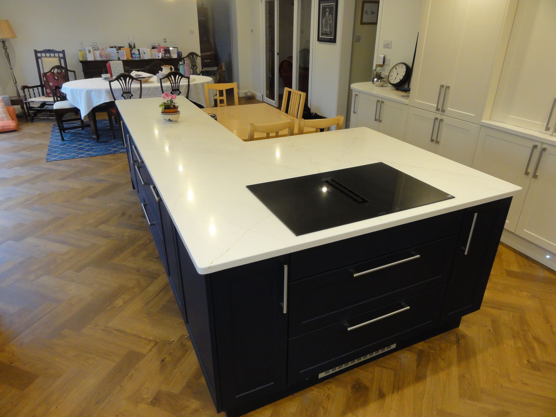 A kitchen island with a white countertop and black base cabinets sits on a herringbone wood floor in a modern kitchen.
