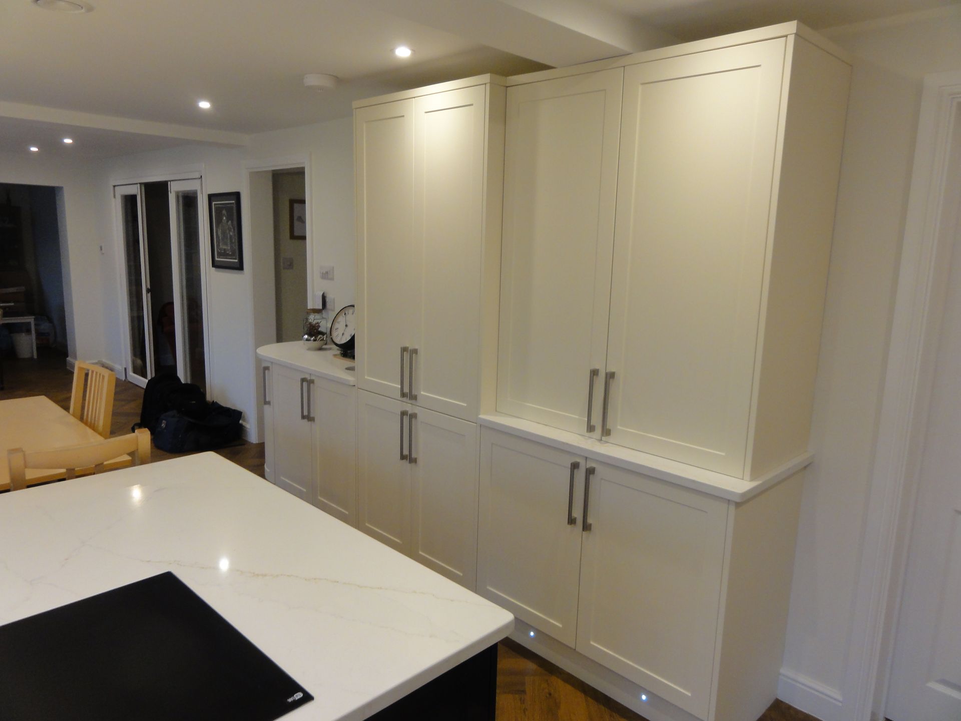Cream-colored kitchen cabinets with silver handles installed along a wall next to a kitchen island with a white countertop.