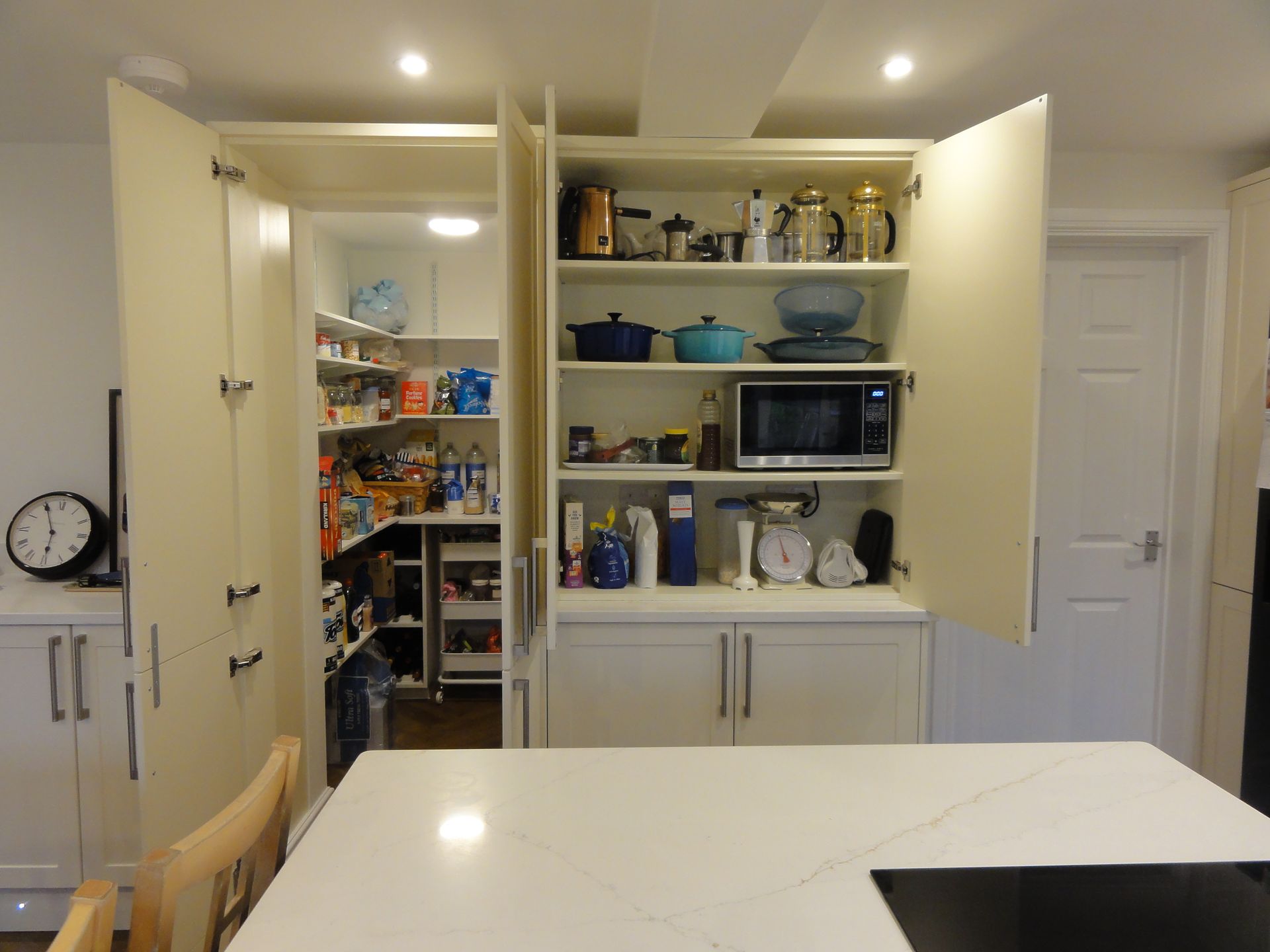 A kitchen featuring an open walk-in pantry next to a cabinet displaying cookware and a microwave, with a center island.
