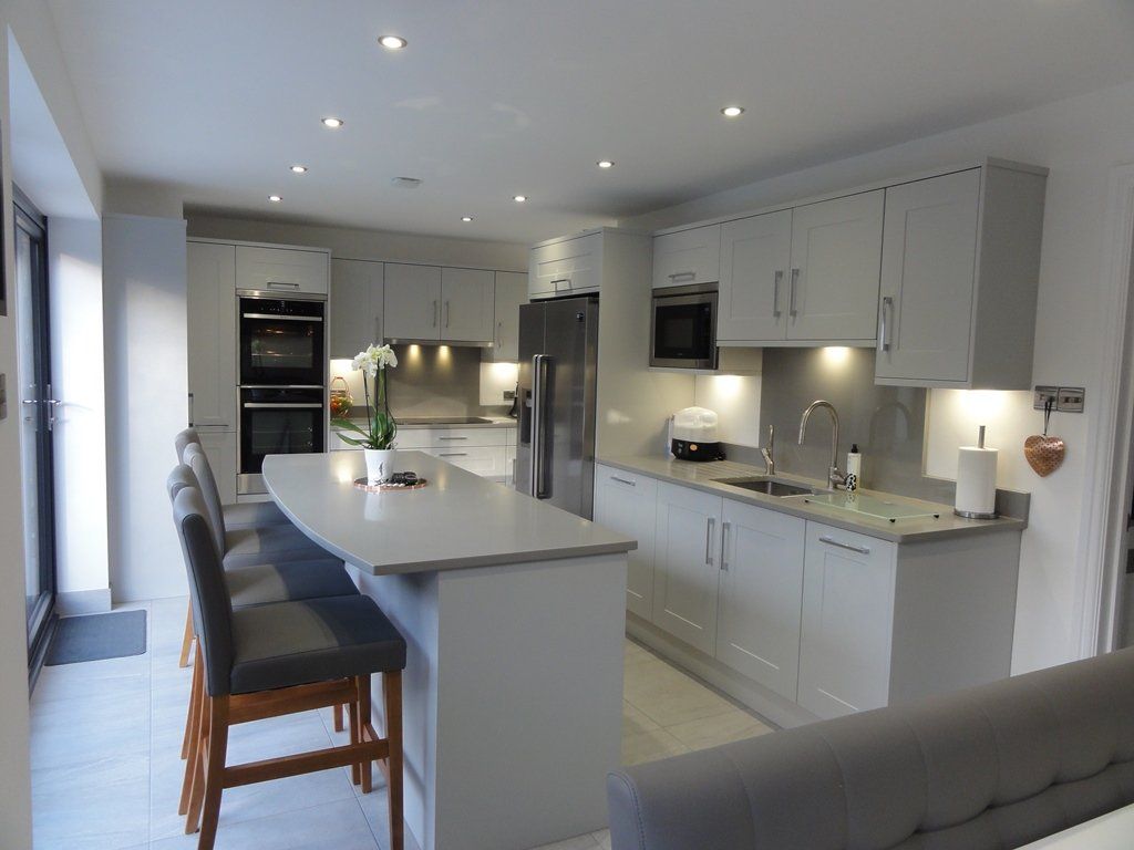 Modern, light-gray kitchen with an island, bar stools, stainless steel appliances, and under-cabinet lighting.
