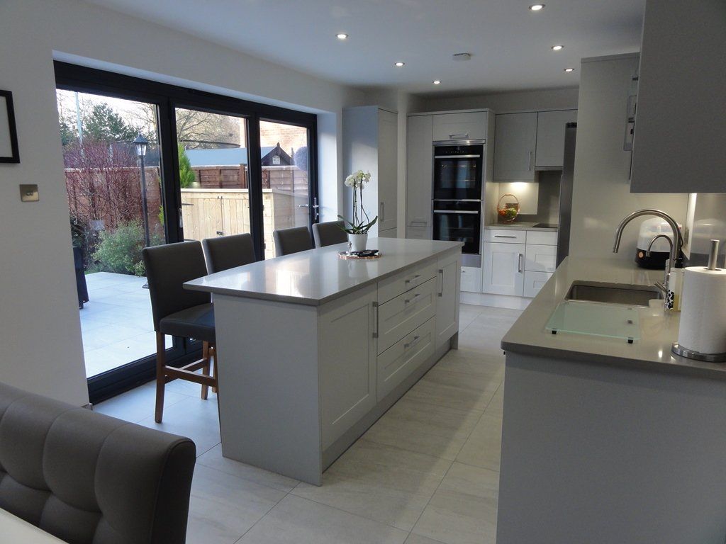 A modern kitchen featuring a gray island with seating, white cabinets, stainless steel appliances, and patio doors.