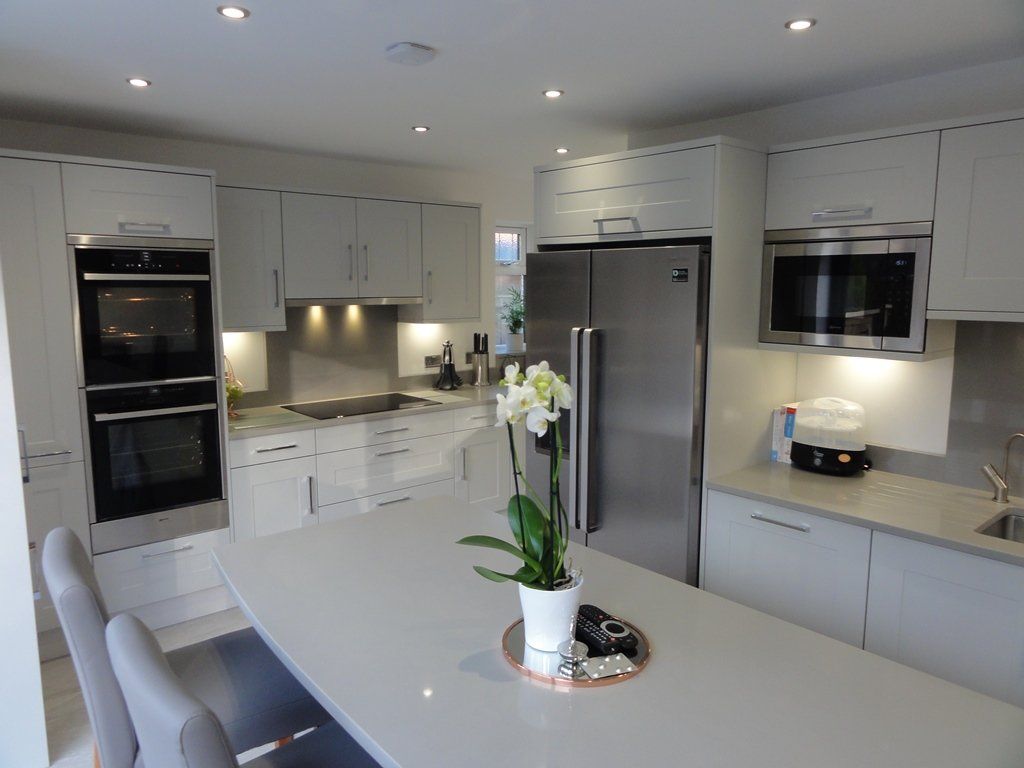 A bright, modern kitchen with light gray cabinets, stainless steel appliances, and a central island topped by a plant.