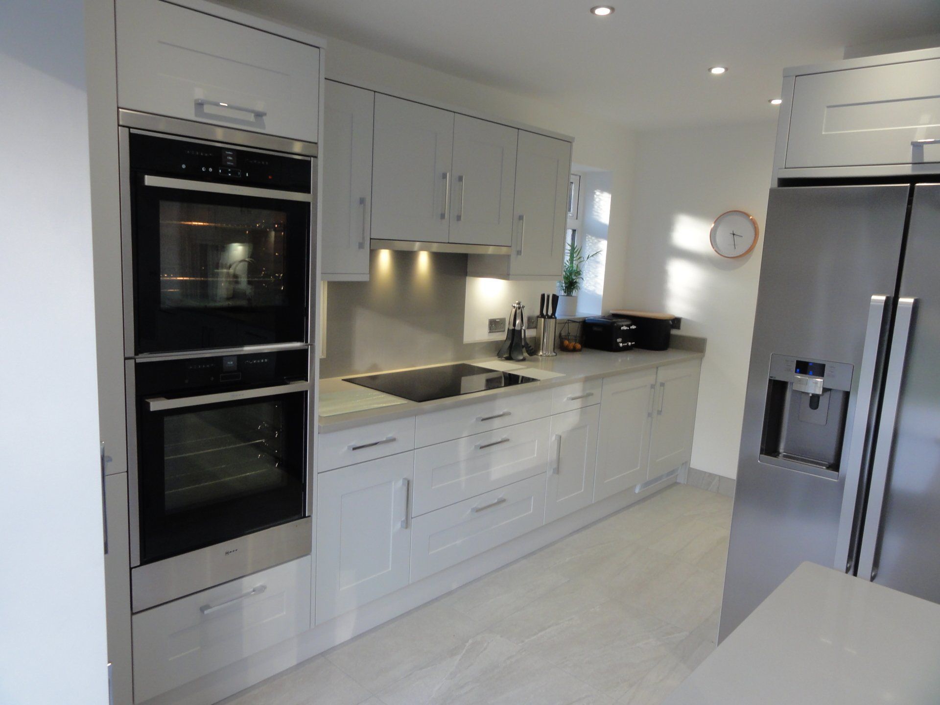 Modern kitchen with light grey cabinets, a stainless steel double oven, induction cooktop, and a matching refrigerator.