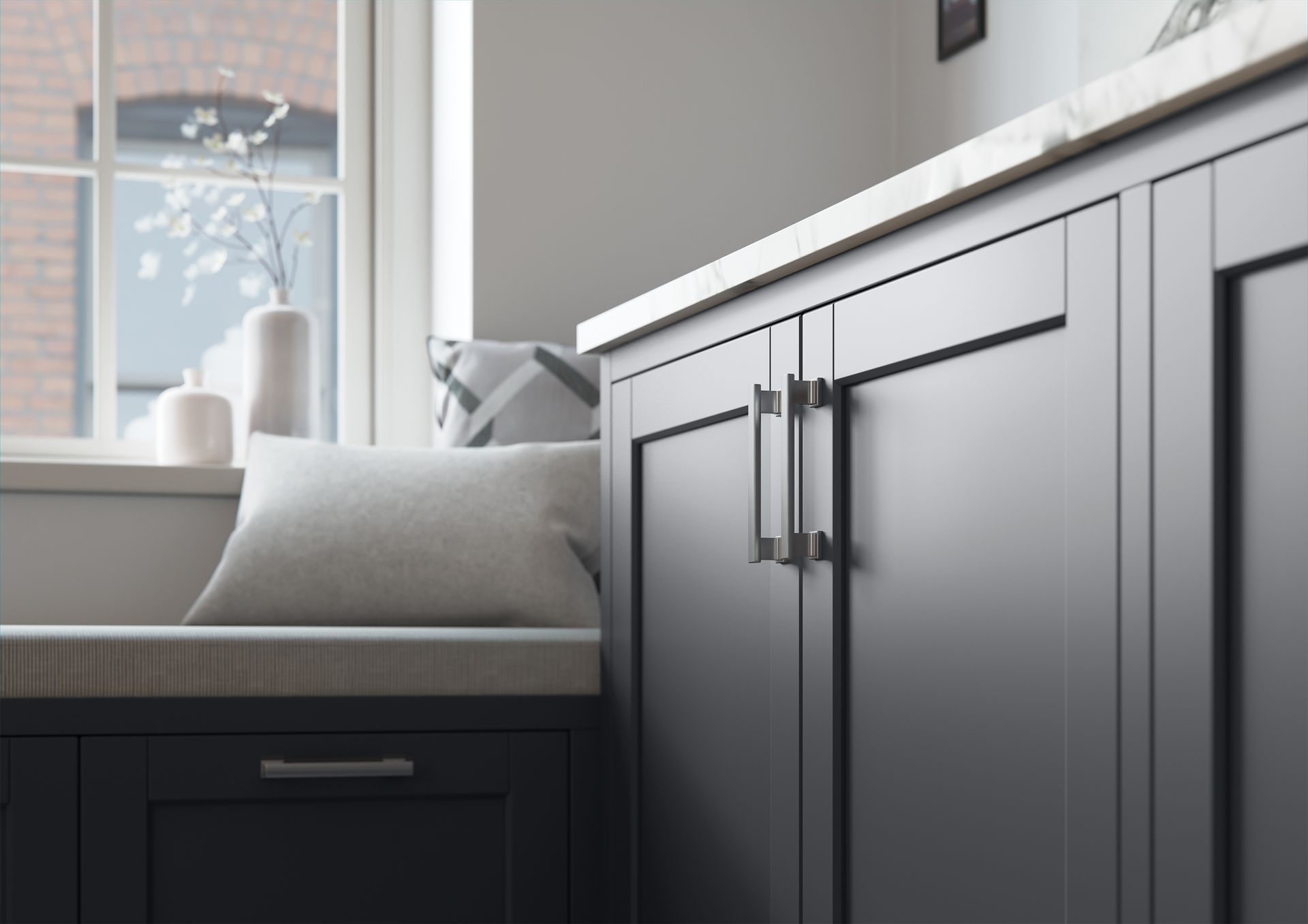 A close-up of dark grey kitchen cabinets with metal pulls, set next to a window seat with a light-colored pillow.