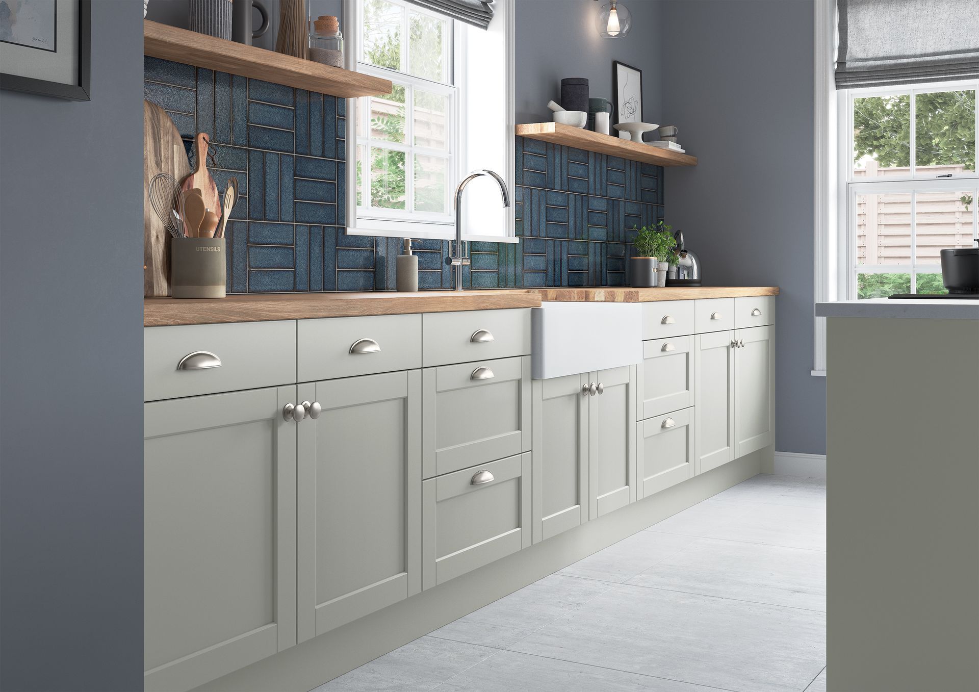 A modern kitchen with light grey cabinets, a white farmhouse sink, natural wood countertops, and blue patterned tile.