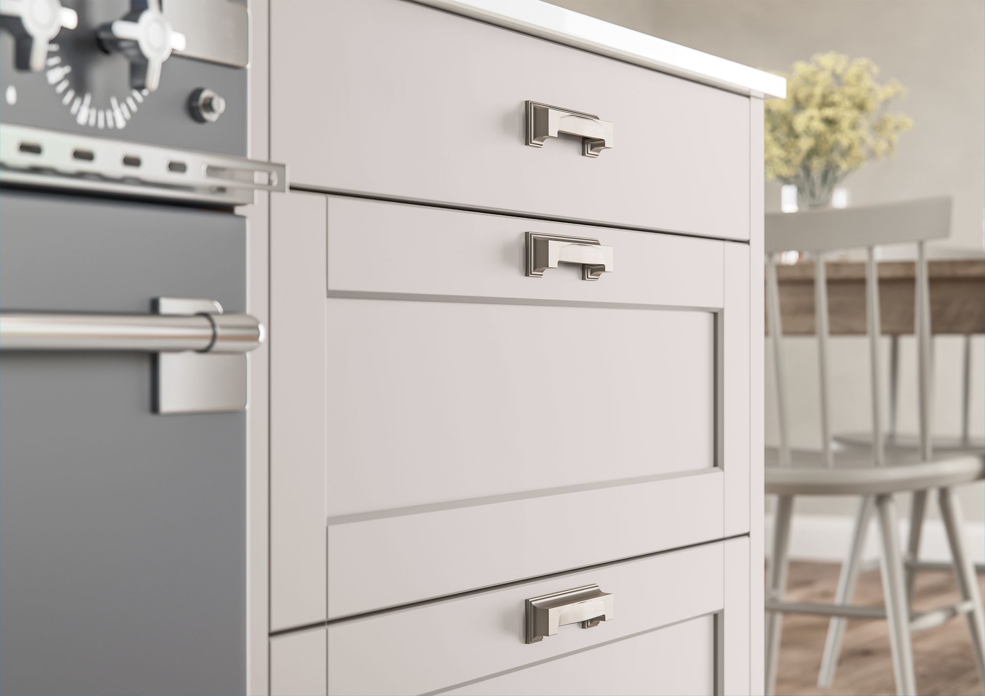 Light gray kitchen cabinetry with polished metal handles positioned beside a gray stove in a bright room.