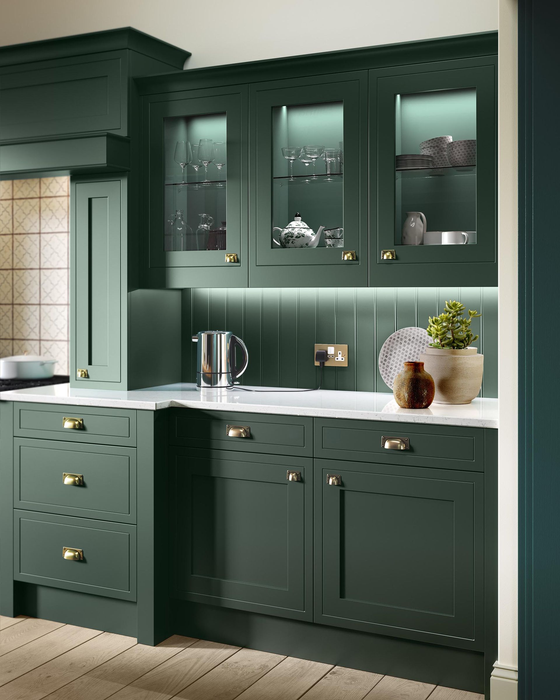 Dark green built-in kitchen cabinets with glass upper doors, white countertop, and decorative jars and plants
