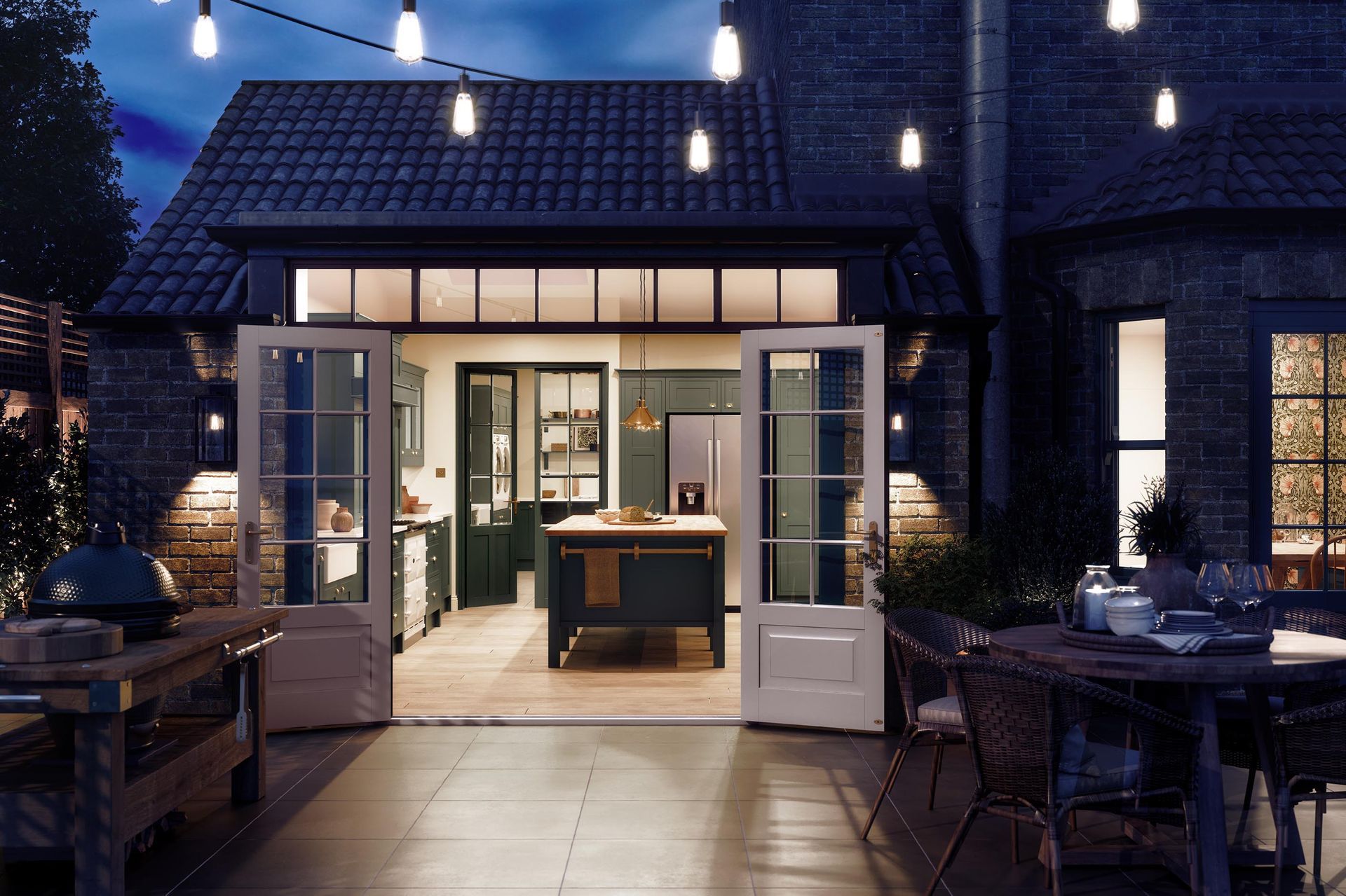 A nighttime view from a patio into a lit kitchen through open French doors, with bistro lights hanging above.