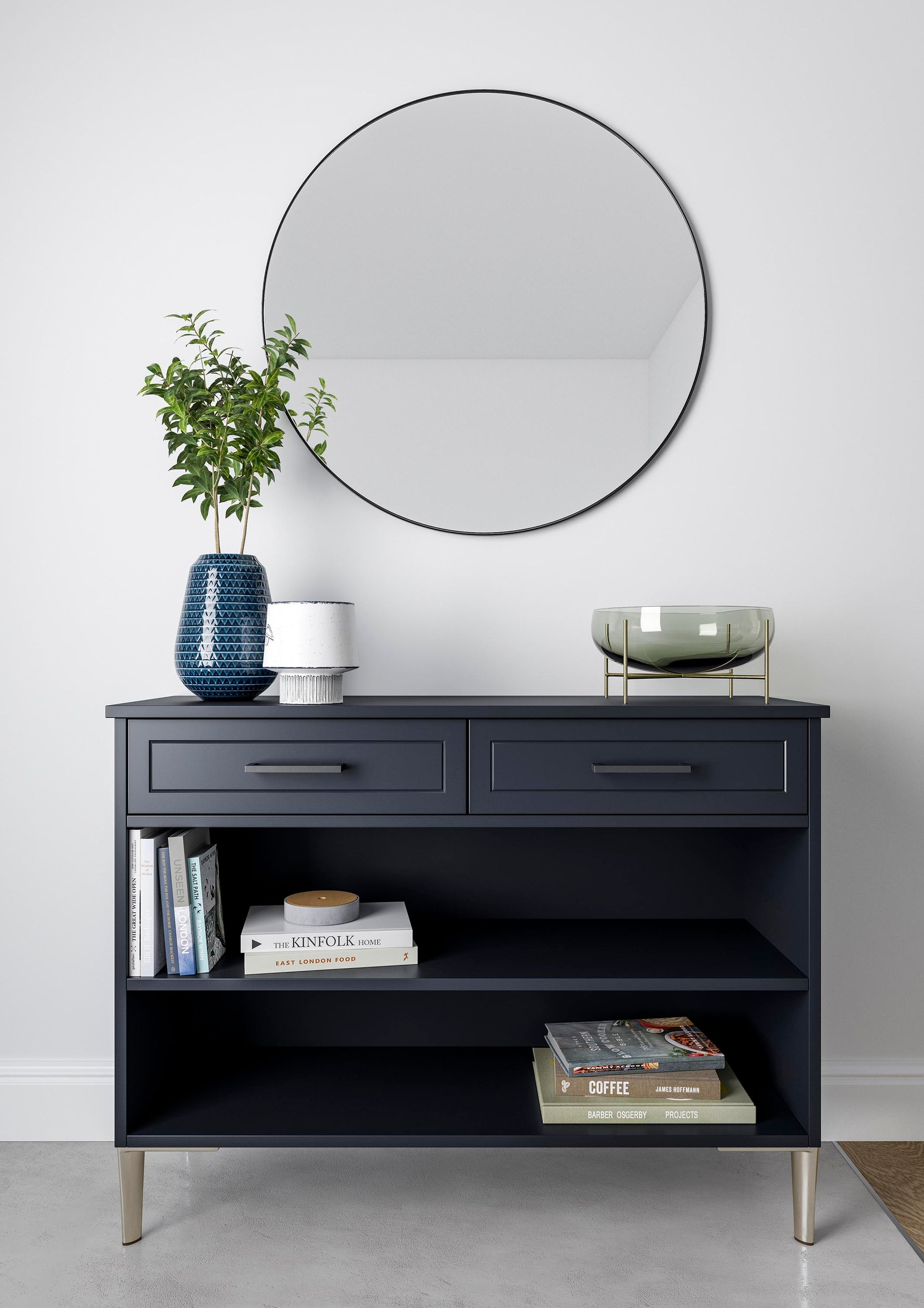 A navy blue console table with drawers and open shelves, topped with a plant, vase, and bowl, under a circular mirror.
