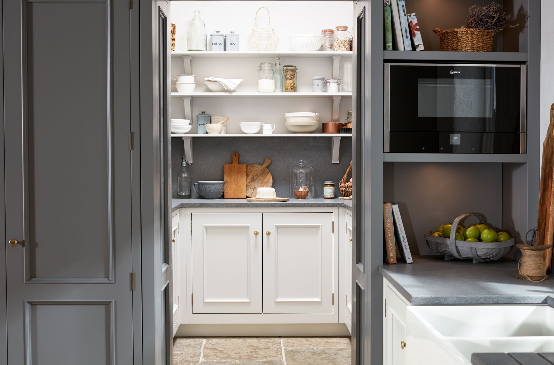 A view through a gray doorway into a kitchen pantry with white cabinets, open shelves, and a built-in microwave nearby.