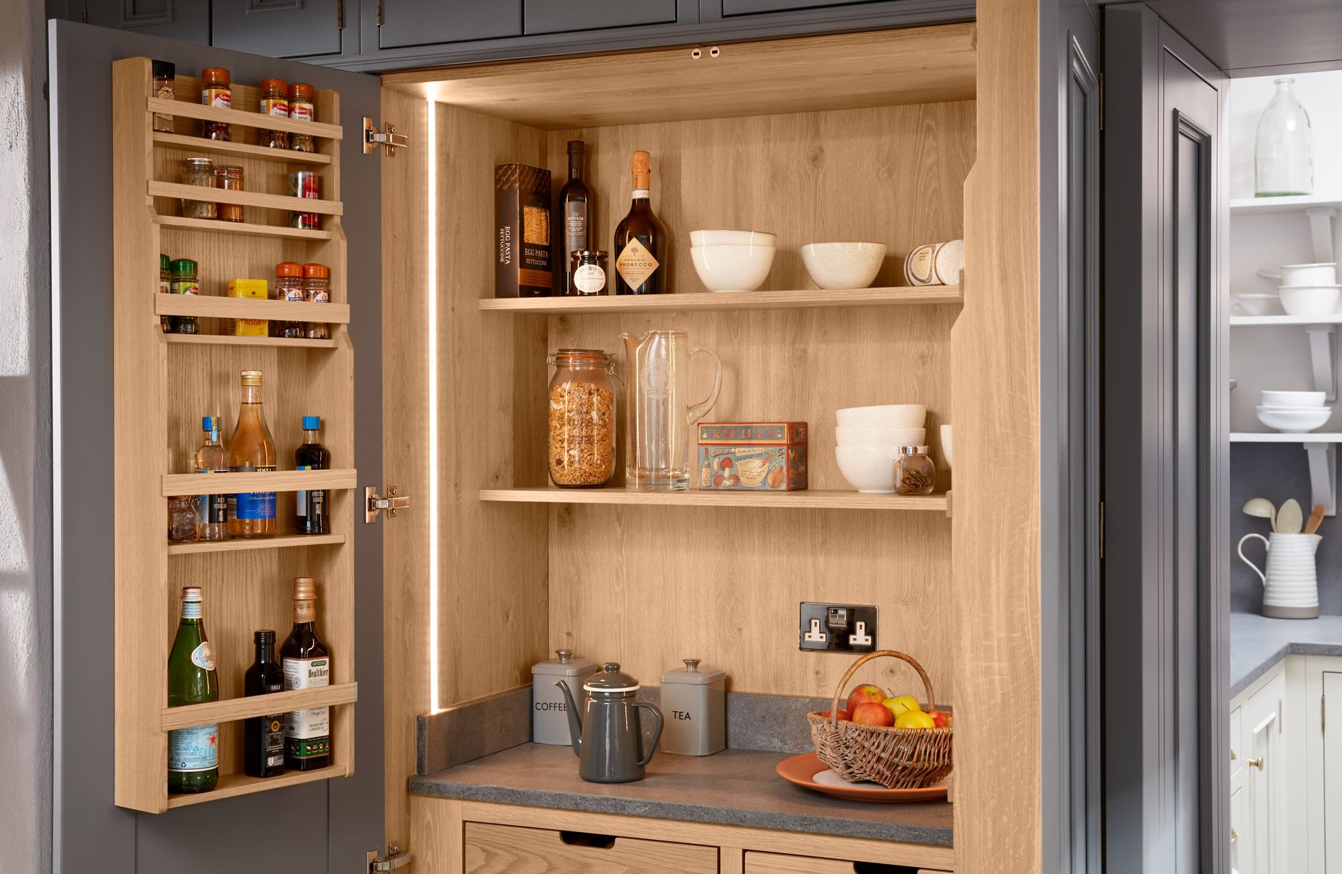 Open dark gray pantry cabinet with light wood interior, door-mounted spice racks, shelves, and a stone countertop.