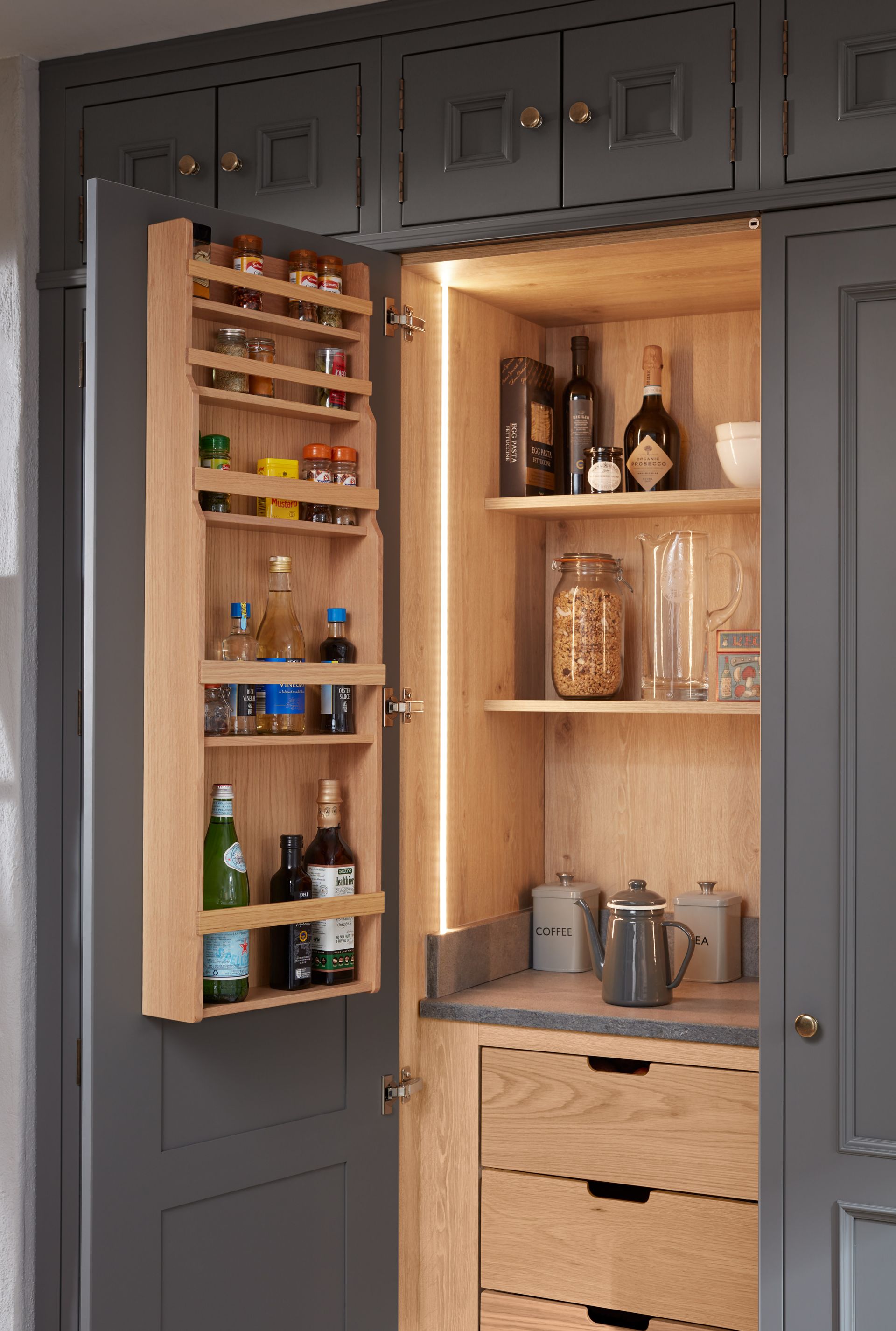 Open dark grey pantry cabinet with built-in wooden door spice racks, shelves, and drawers, lit by internal LED strips.