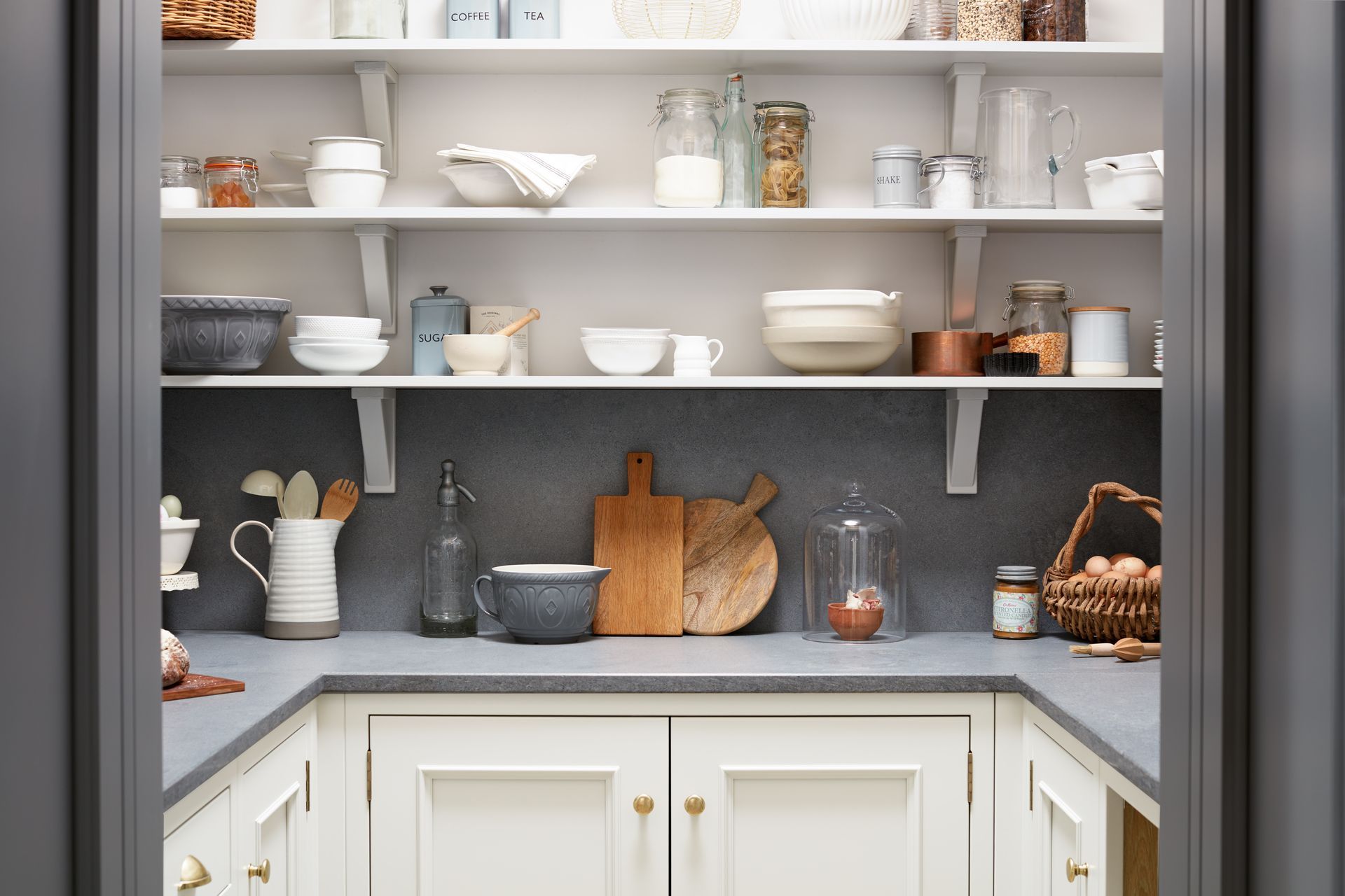 A well-organized pantry featuring white shelving, light countertops, and cabinetry with various kitchenware and utensils.