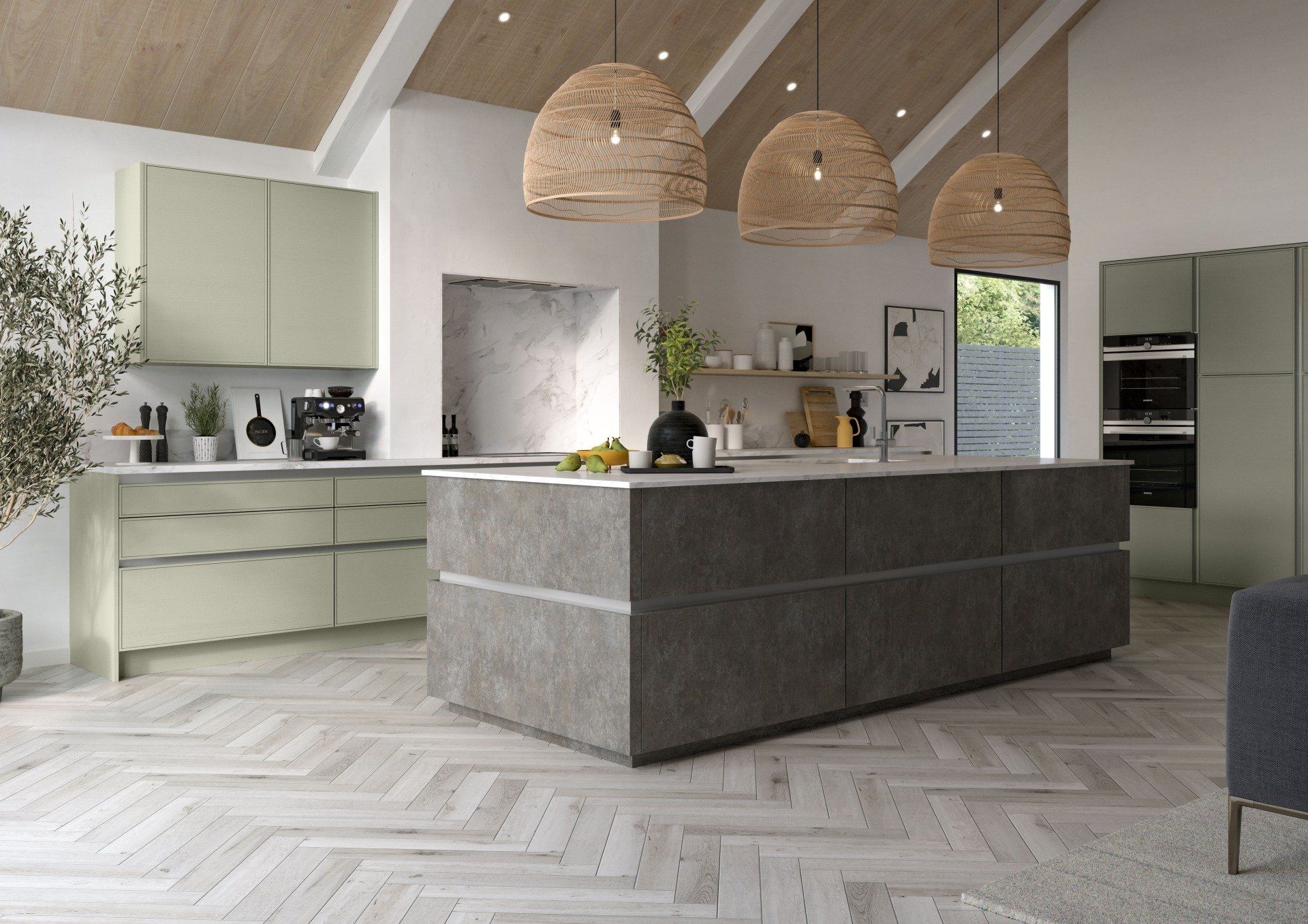 A modern kitchen with sage green cabinets, a large dark stone island, wicker pendant lights, and light herringbone floors.