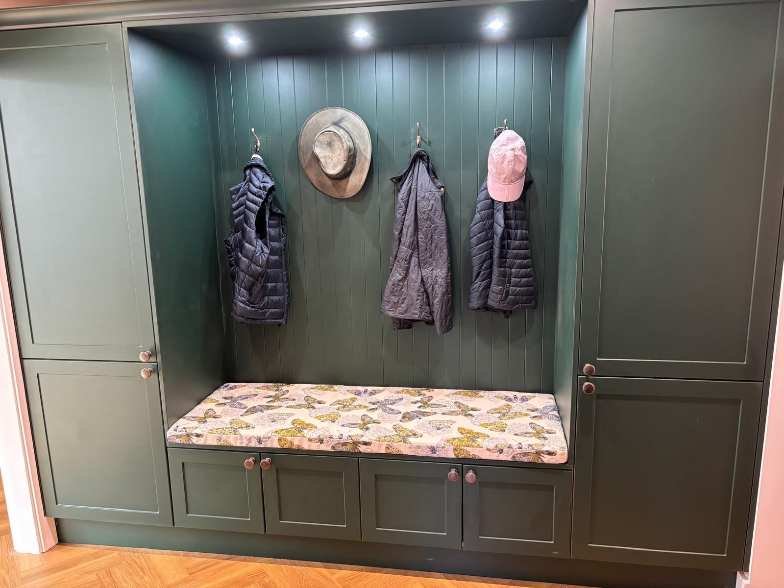 Dark green built-in mudroom entryway with lockers, coat hooks, and a bench with a floral cushion.