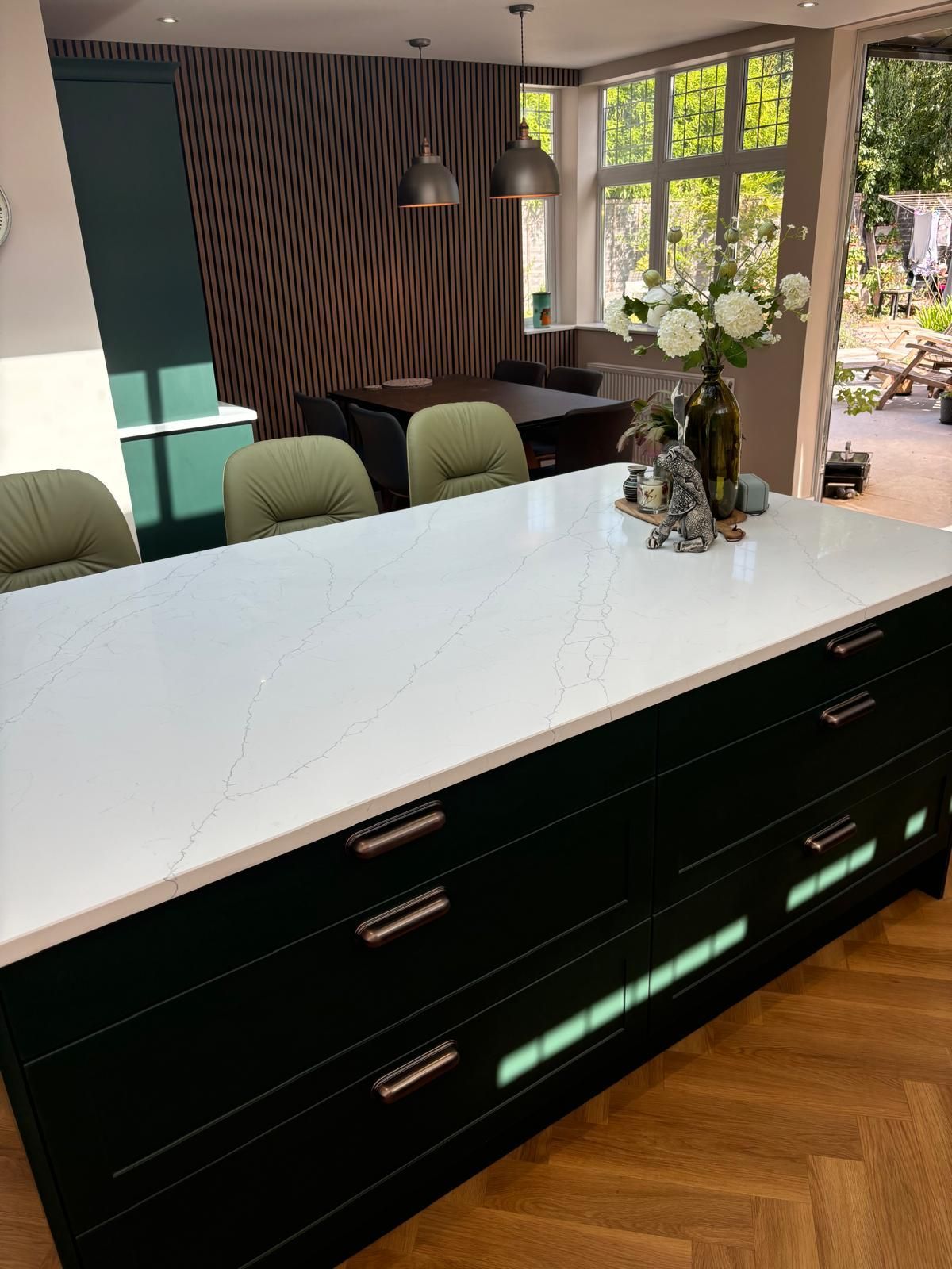 A modern kitchen island with dark cabinetry and a white marble-patterned countertop, featuring green chairs and decor.