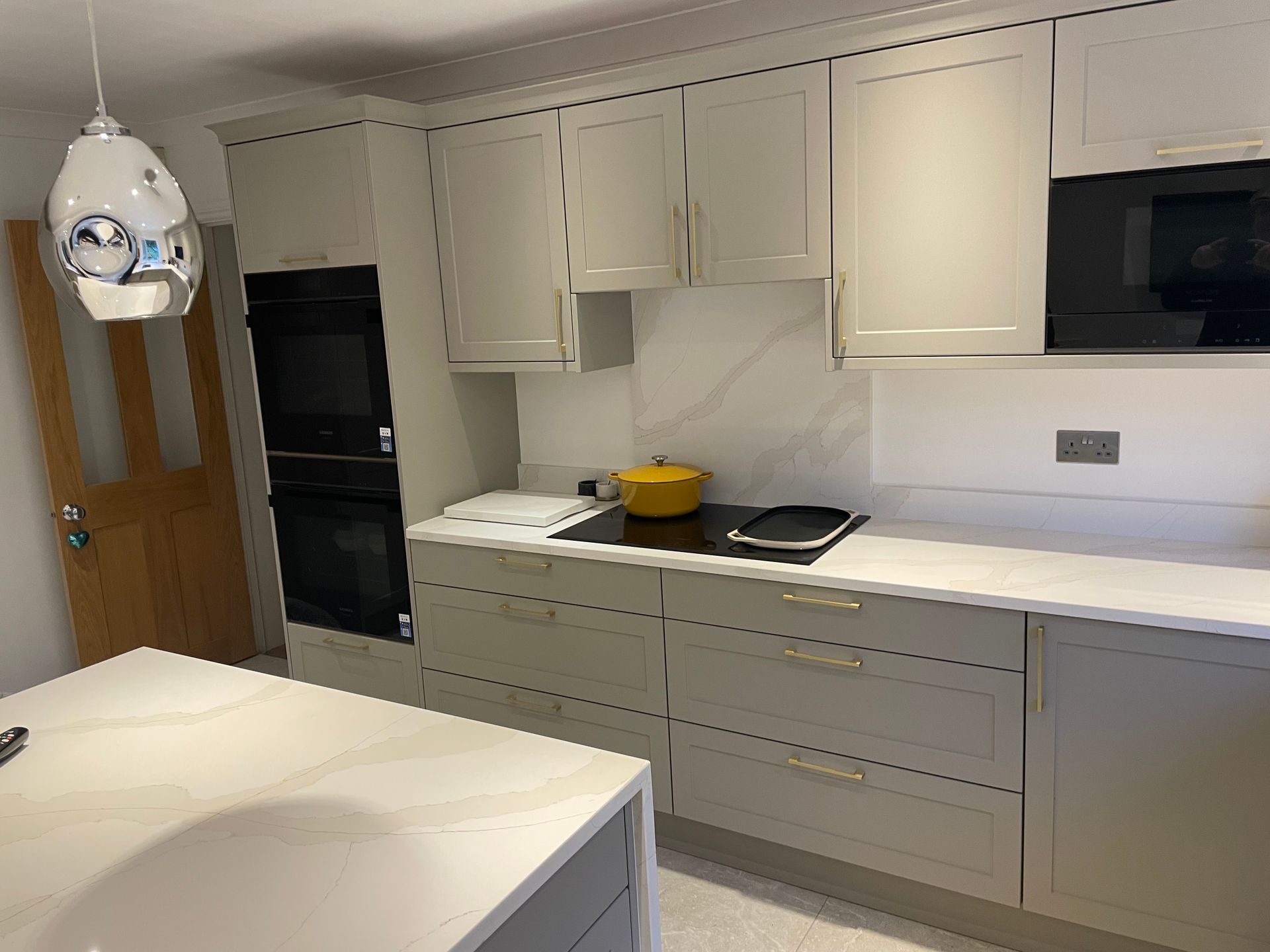 A modern, neutral-toned kitchen featuring light gray cabinetry, white marble countertops, and a built-in oven unit.