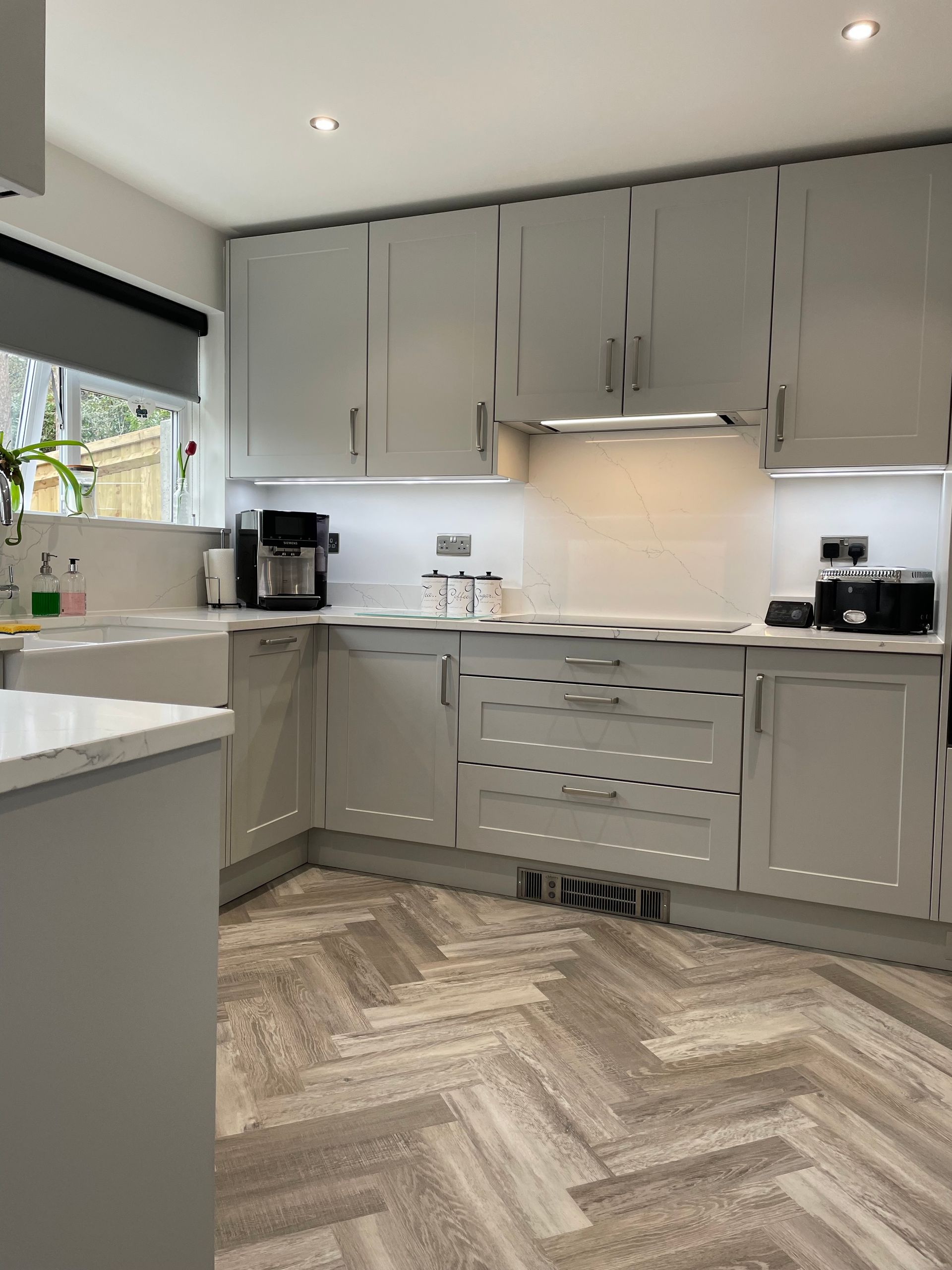 Modern gray kitchen with white countertops, herringbone wood floor, and built-in cabinets