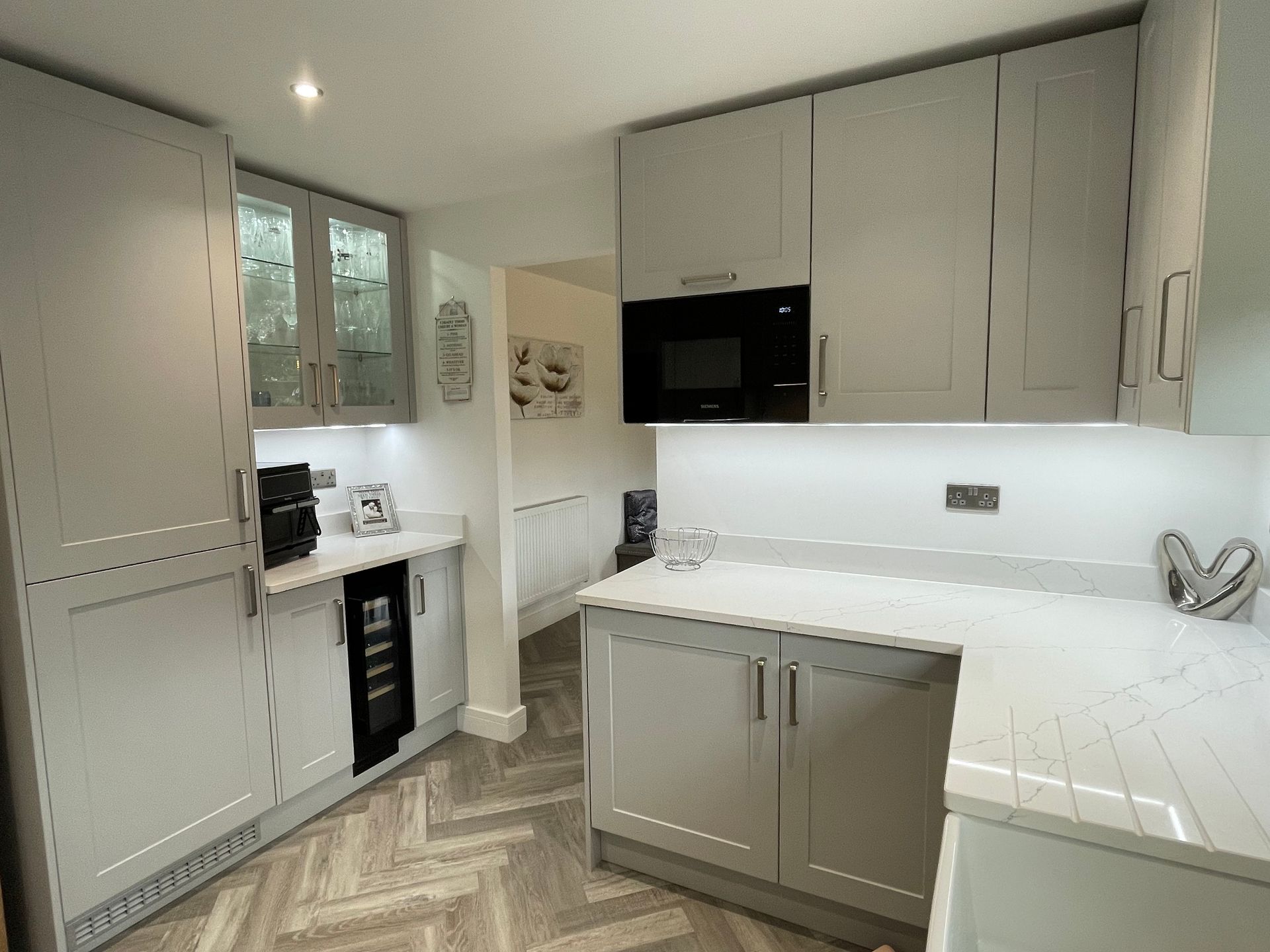 Bright modern kitchen with white cabinets, marble countertops, black appliances, and herringbone wood flooring