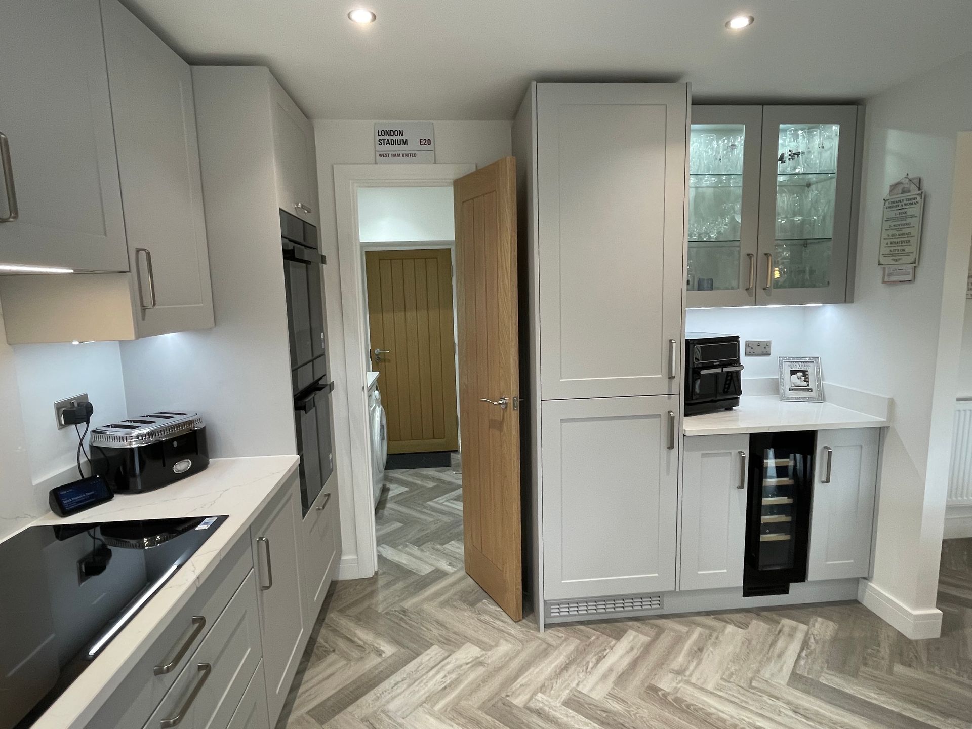 Modern white kitchen with gray cabinets, built-in appliances, and an open door to a hallway.