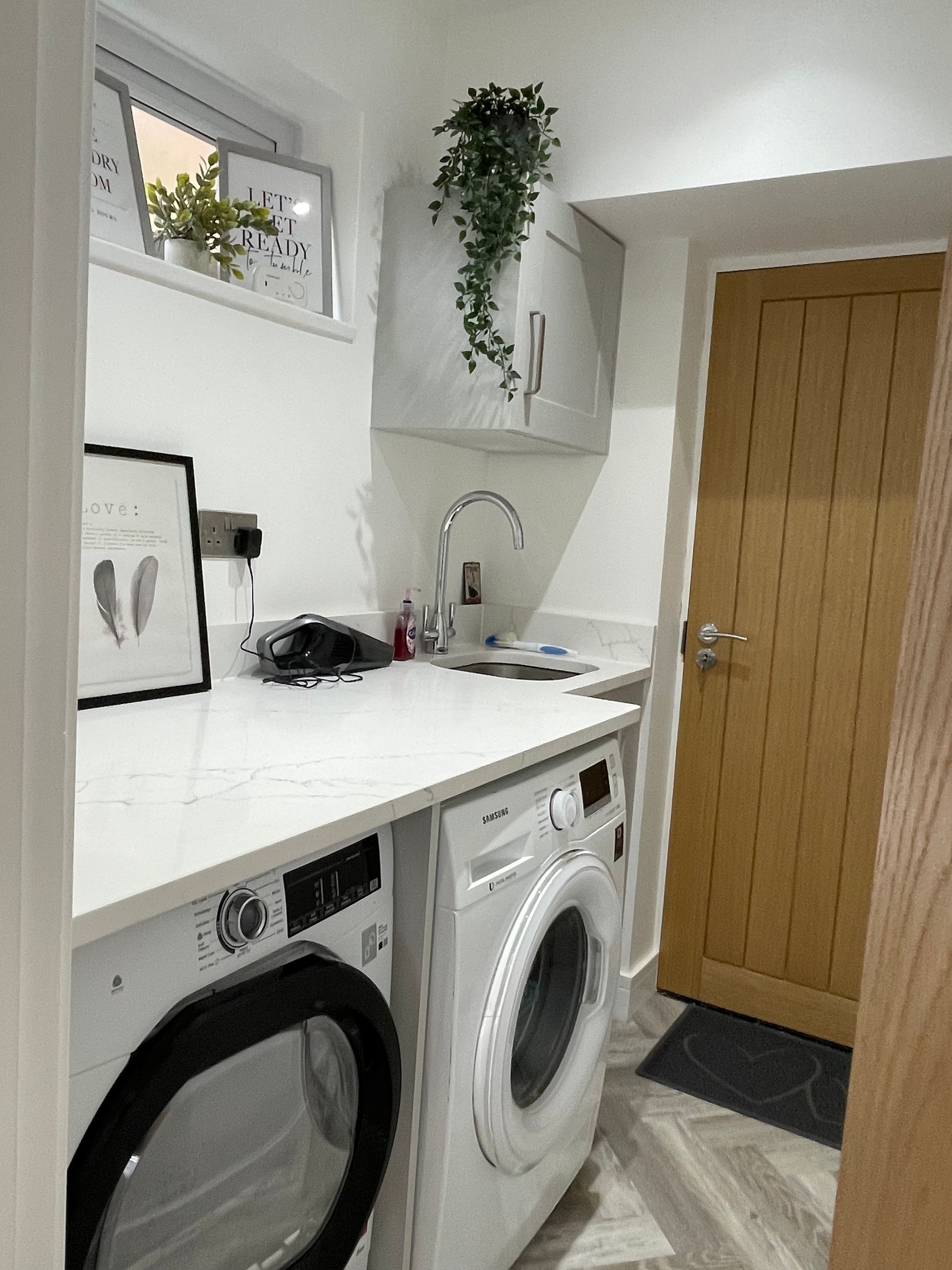 Bright laundry room with washer, dryer, white countertop, sink, and tan door on the right