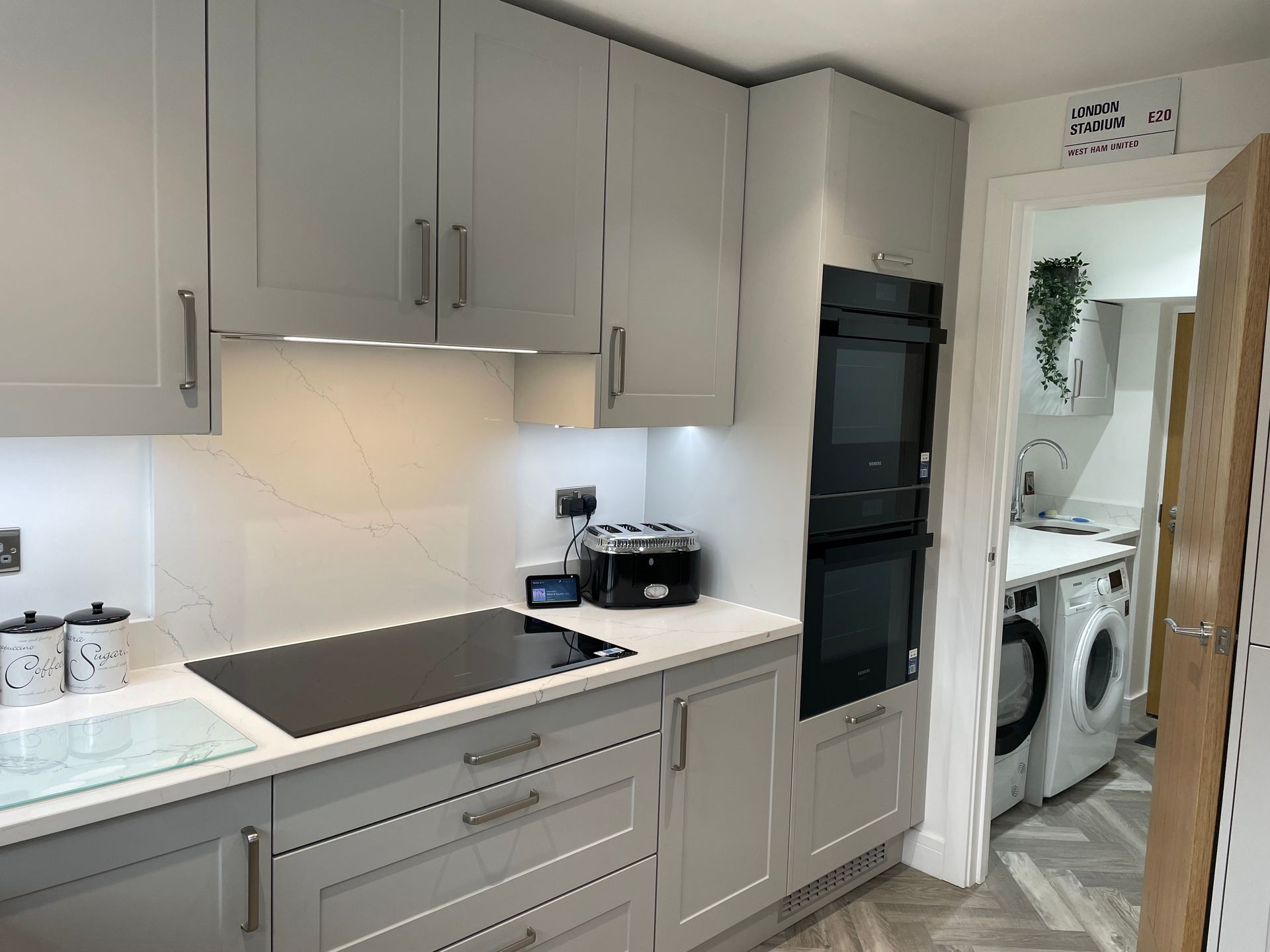 Modern gray kitchen with built-in oven, black cooktop, and doorway to a laundry room with washer and dryer