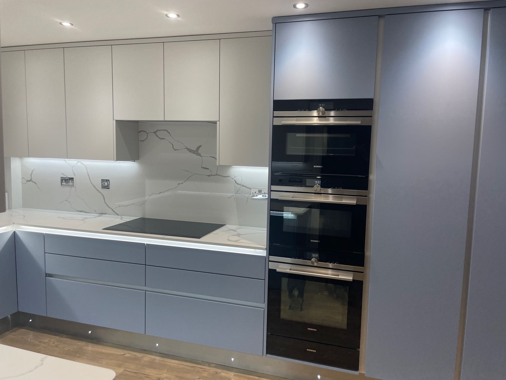 A modern kitchen featuring blue and white cabinets, marble-patterned backsplash, and a built-in double oven.