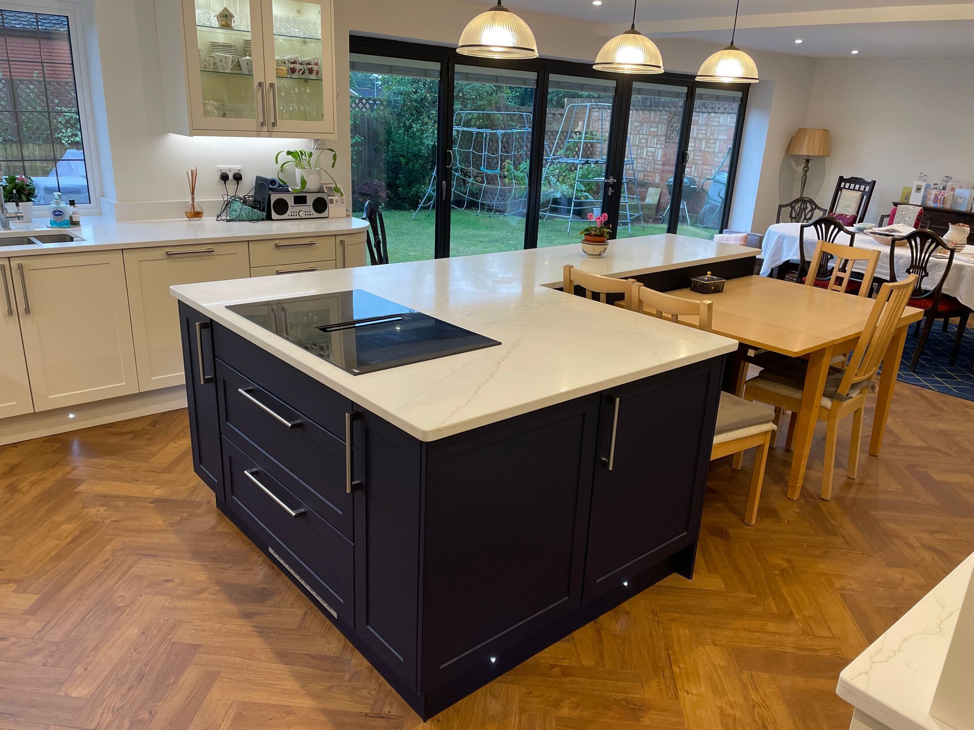 A dark blue kitchen island with a white countertop and stovetop sits in a kitchen with parquet wood floors.