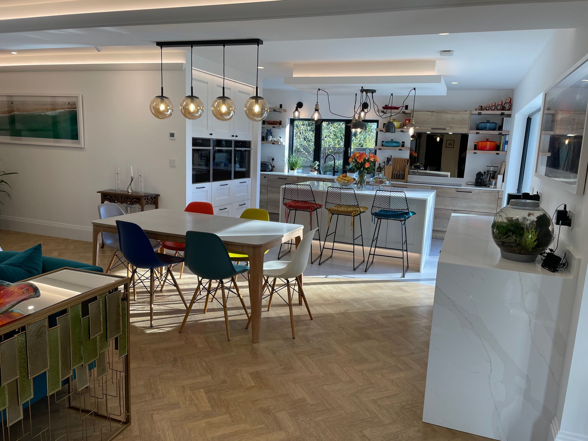 A bright, open-plan kitchen and dining area with parquet floors, colorful chairs, and a white marble-topped island.
