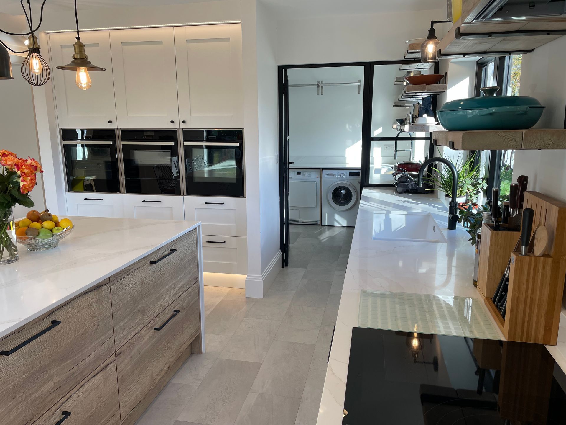 A modern kitchen featuring a wood-grain island, white cabinets, stainless ovens, and an adjacent laundry room.