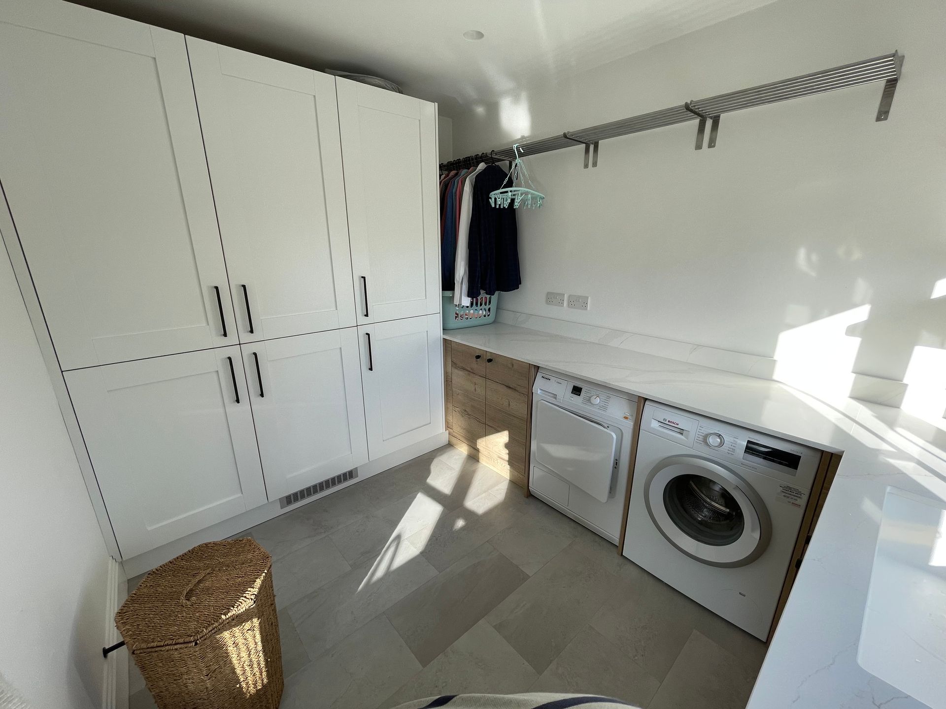 Laundry room with white cabinets, a wicker basket, countertop, clothes rack, washer, and dryer.