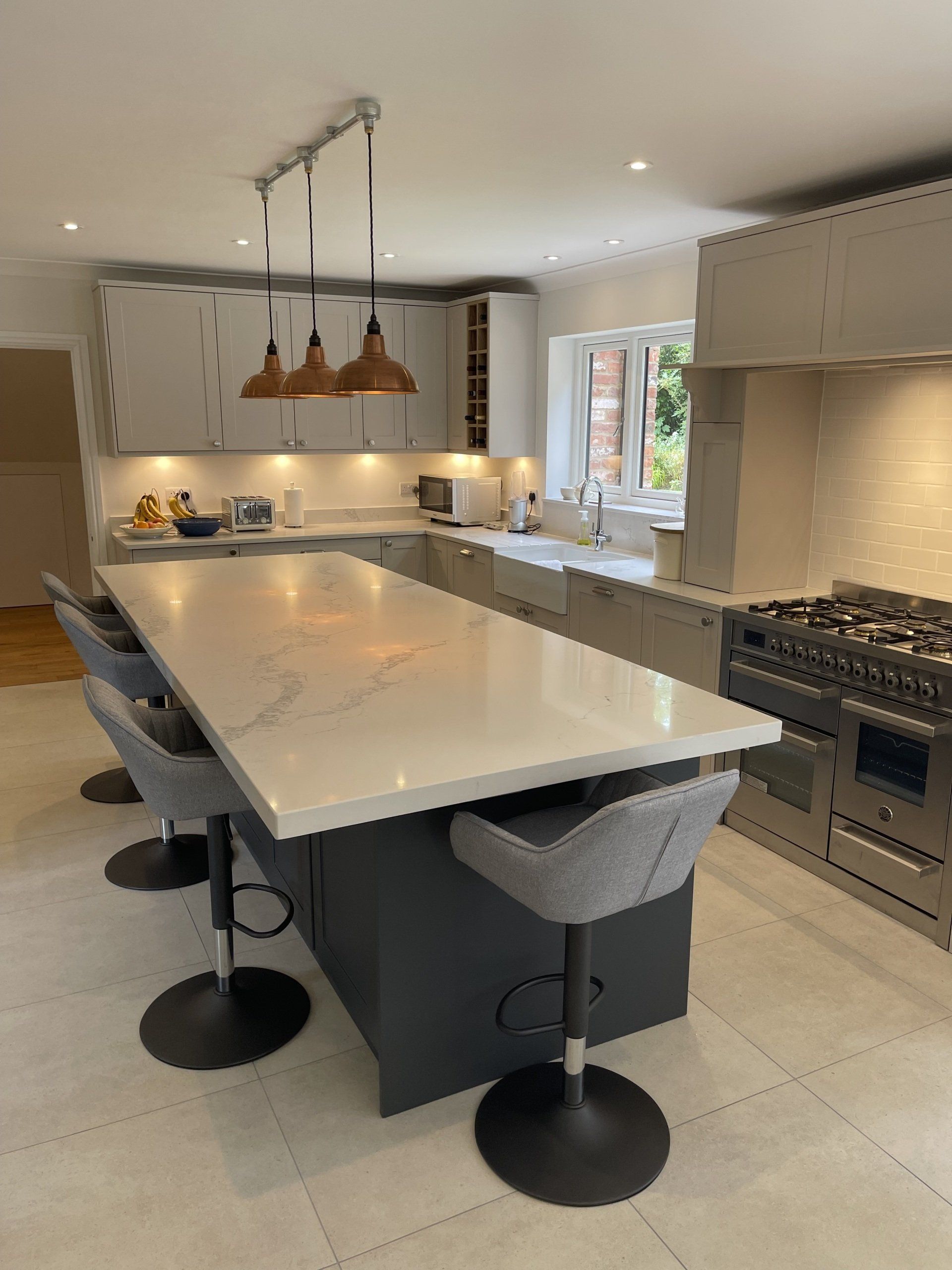 A modern kitchen featuring a dark gray island with marble countertop, four bar stools, and pendant lights over the island.